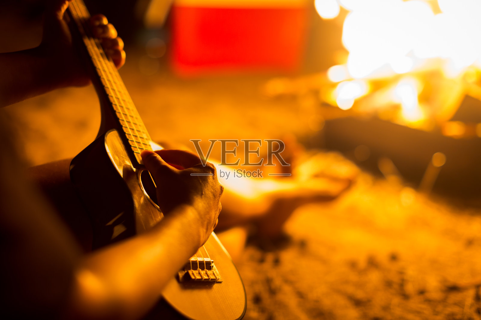 一个人坐在沙滩上的篝火旁，弹吉他放松照片摄影图片