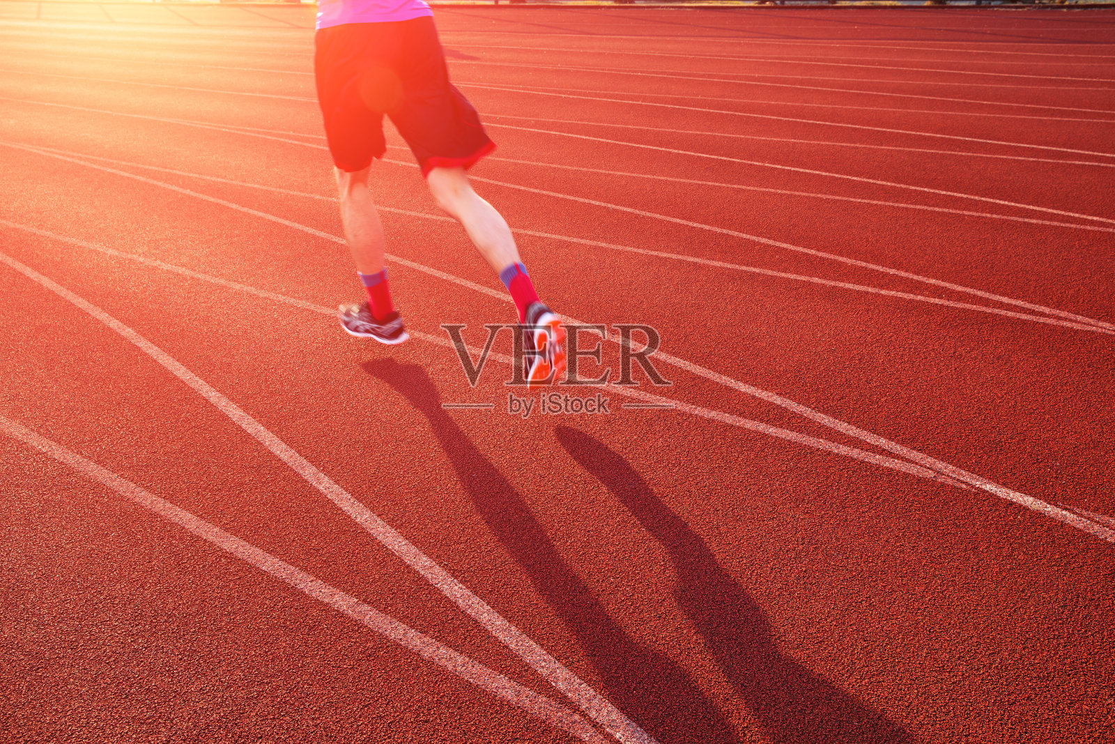 一个年轻人在阳光明媚的早晨在体育场的跑道上跑步照片摄影图片