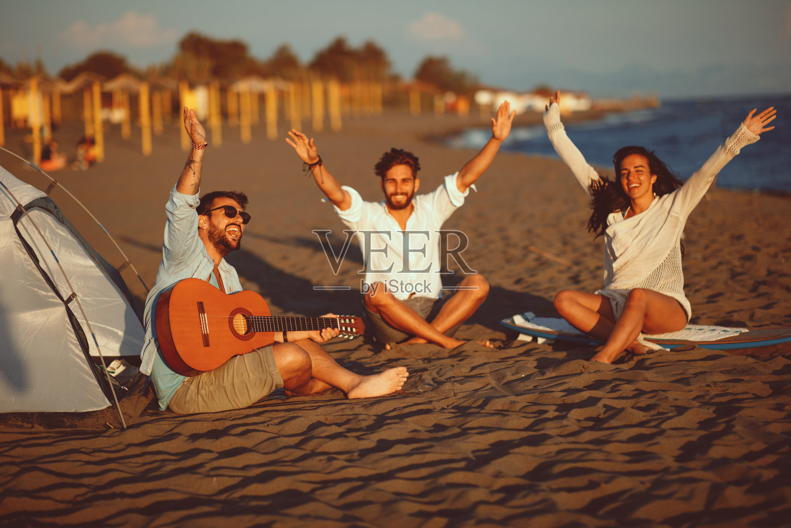 快乐的朋友们坐在海滩上唱着歌，弹着吉他照片摄影图片