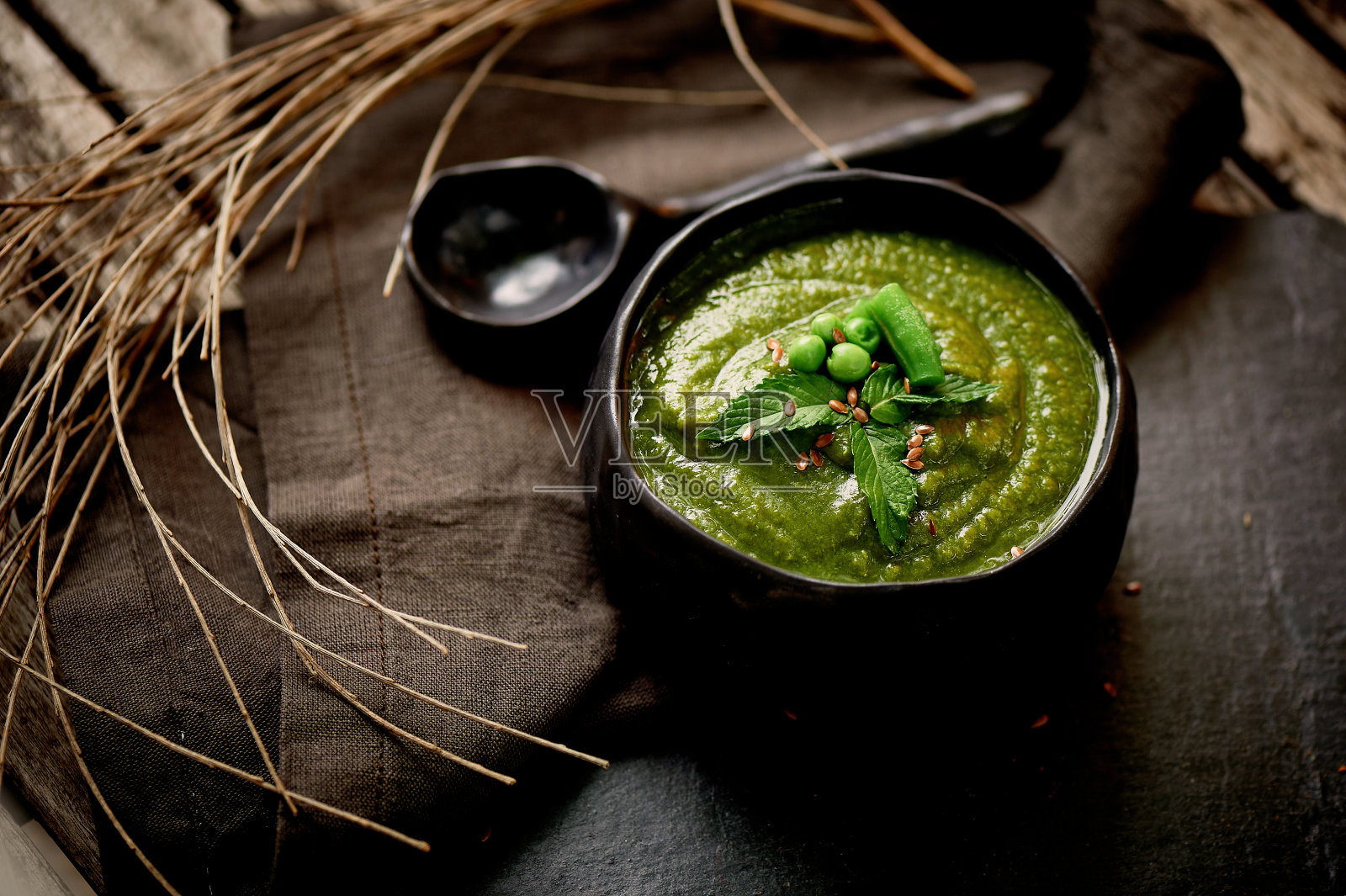 绿色的花椰菜汤，灰色的架子上，木制的背景。乡村风格。简单又营养的素食。装饰着种子。用亚麻餐巾。用干树枝照片摄影图片