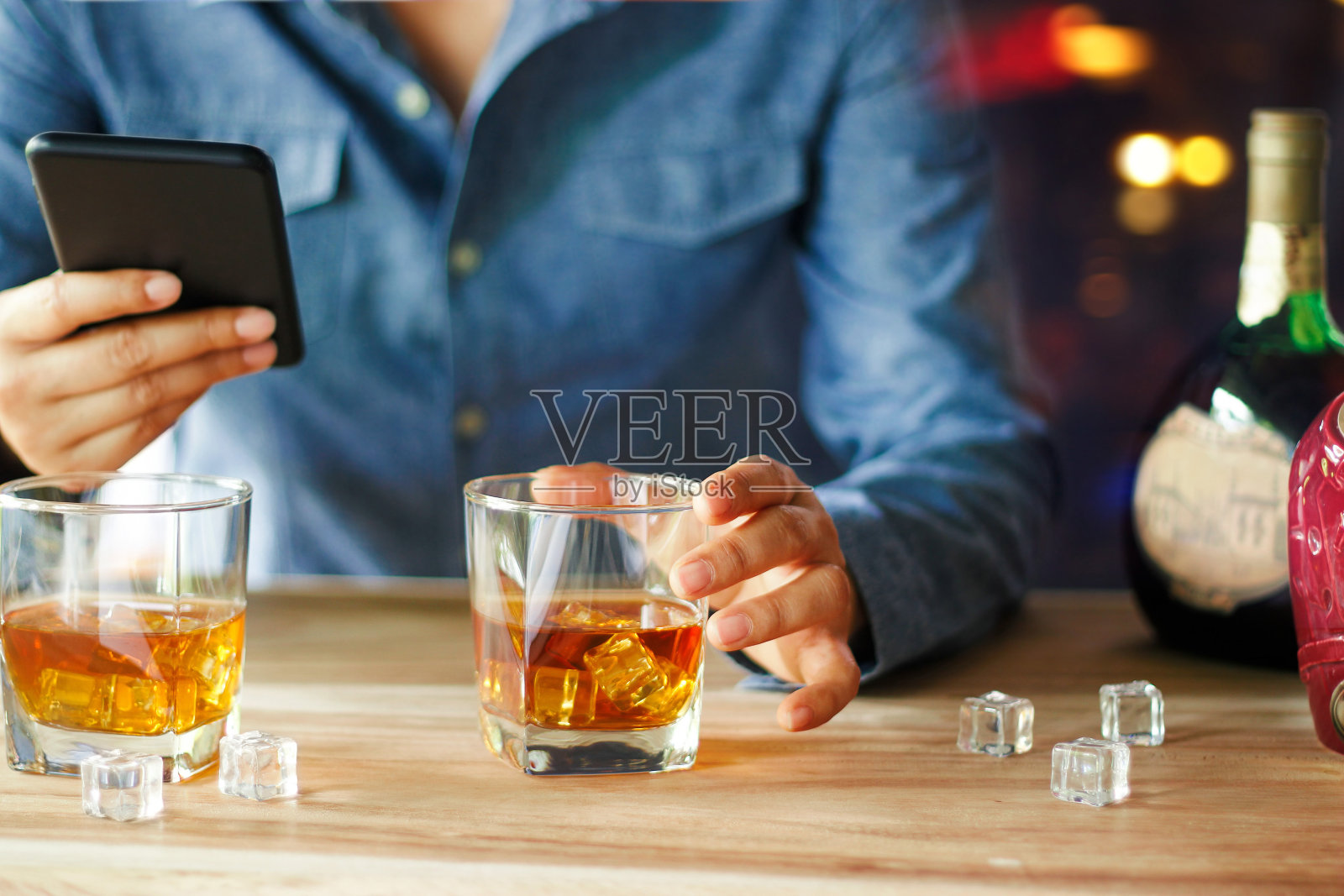 一名男子在酒吧柜台边喝威士忌酒精饮料边使用智能手机。照片摄影图片