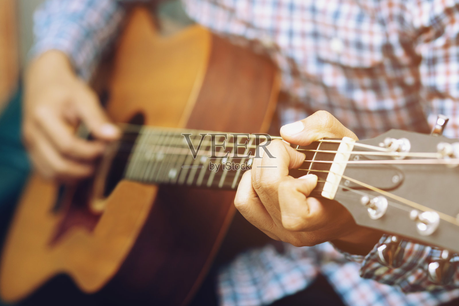 时髦的家伙手弹原声吉他。艺术家年轻的男音乐家格子衬衫演奏吉他在沙发客厅客厅。照片摄影图片