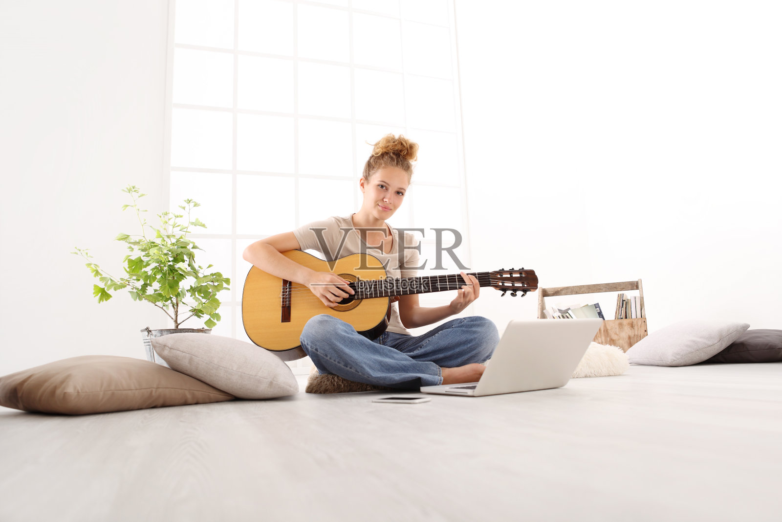 美丽微笑的年轻女子用电脑弹吉他，学习玩在线课程，坐在家里的地板上穿着休闲衣服照片摄影图片