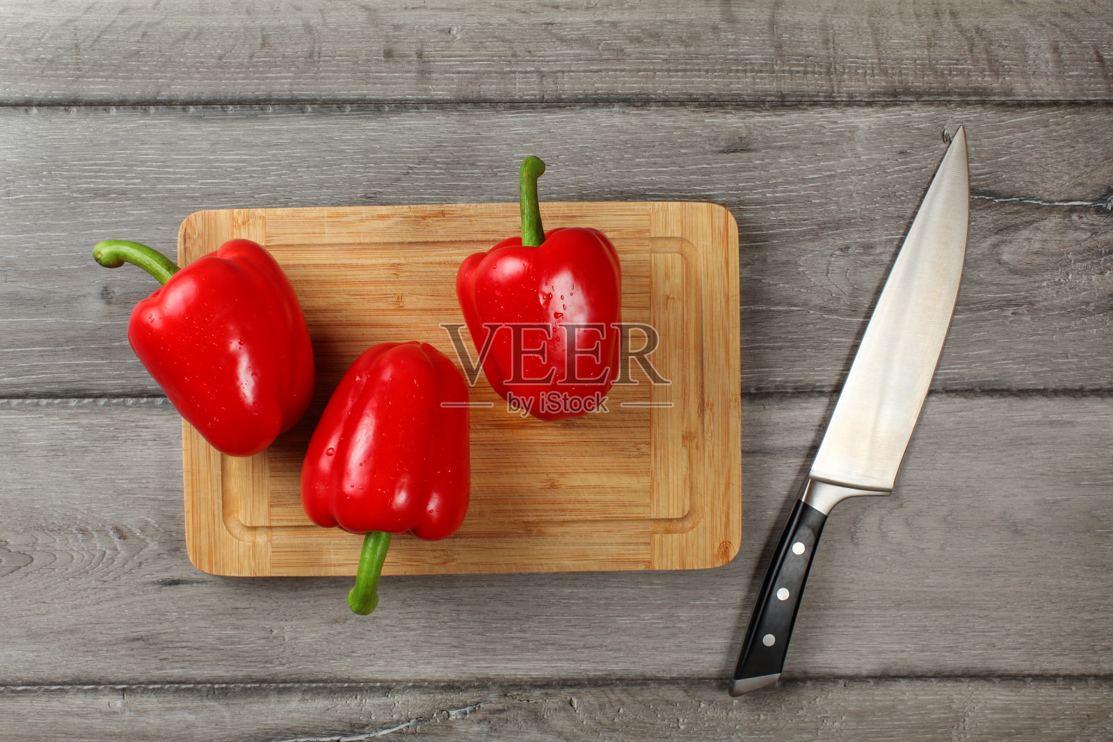 3个红甜椒放在切菜板上，旁边放着刀，准备切。照片摄影图片