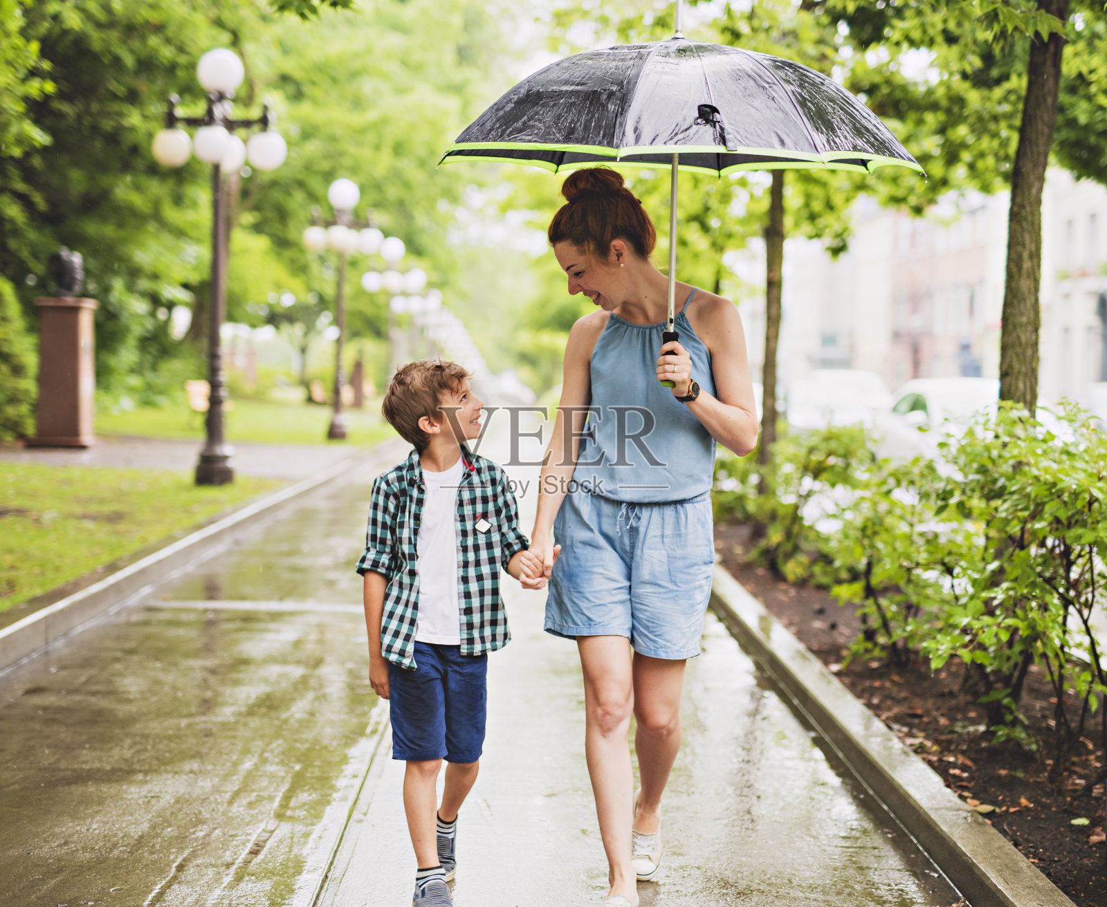 妈妈和孩子在一个下雨天带着伞在公园里照片摄影图片