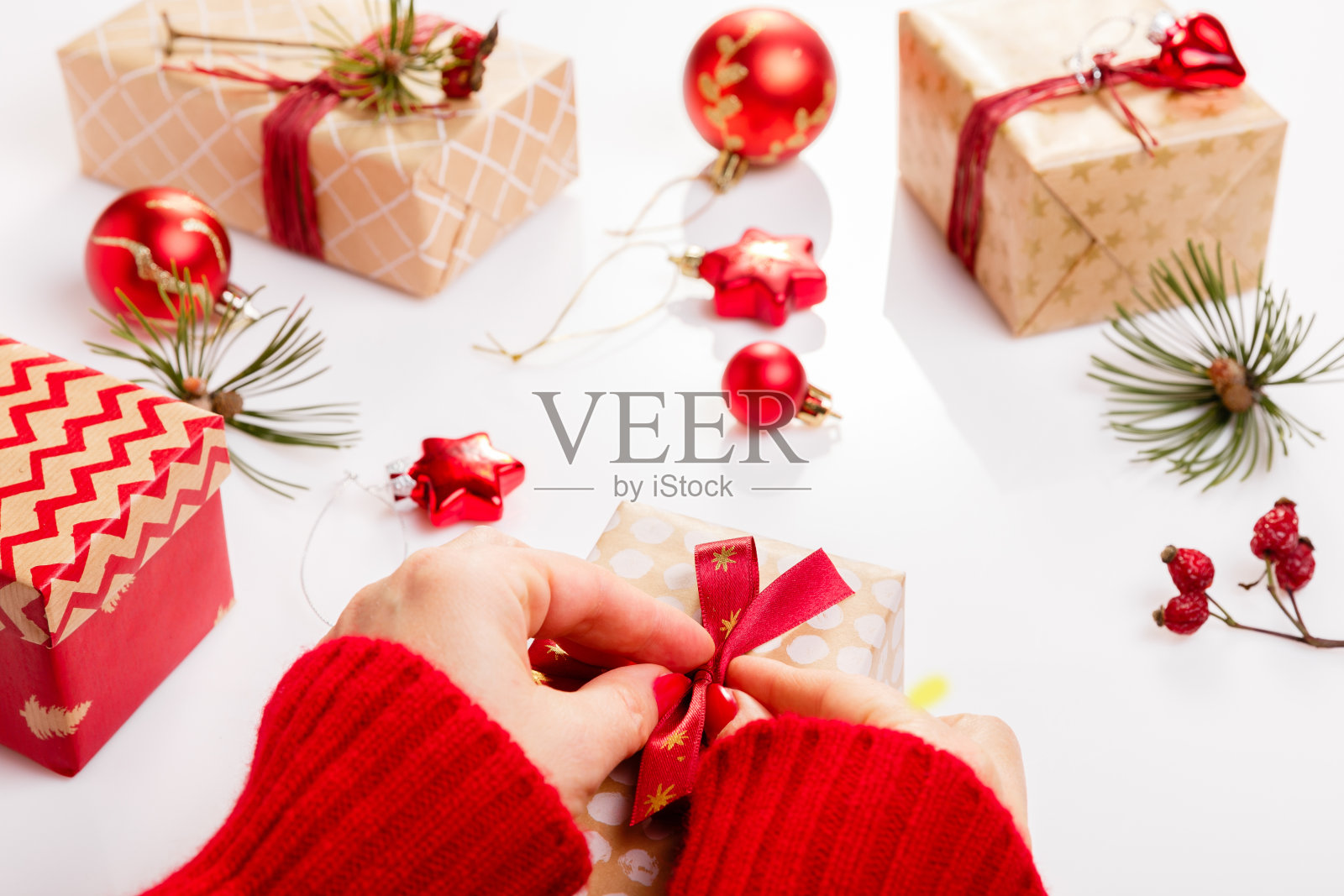 加工包装圣诞礼物。白色木桌用红色装饰，彩球、蜡烛、星星、女手装饰礼品红金色丝带。新的一年，冬天的概念。照片摄影图片