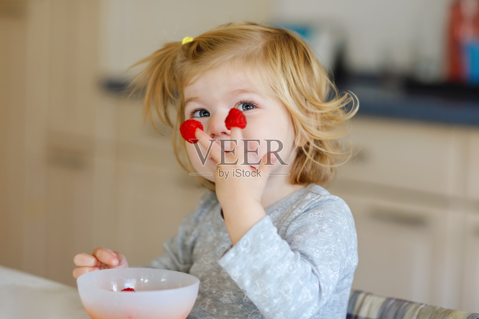 可爱美丽的小女孩正在吃新鲜的树莓。可爱的婴儿品尝覆盆子。健康食品，儿童和发展。快乐的孩子在家或托儿所。照片摄影图片