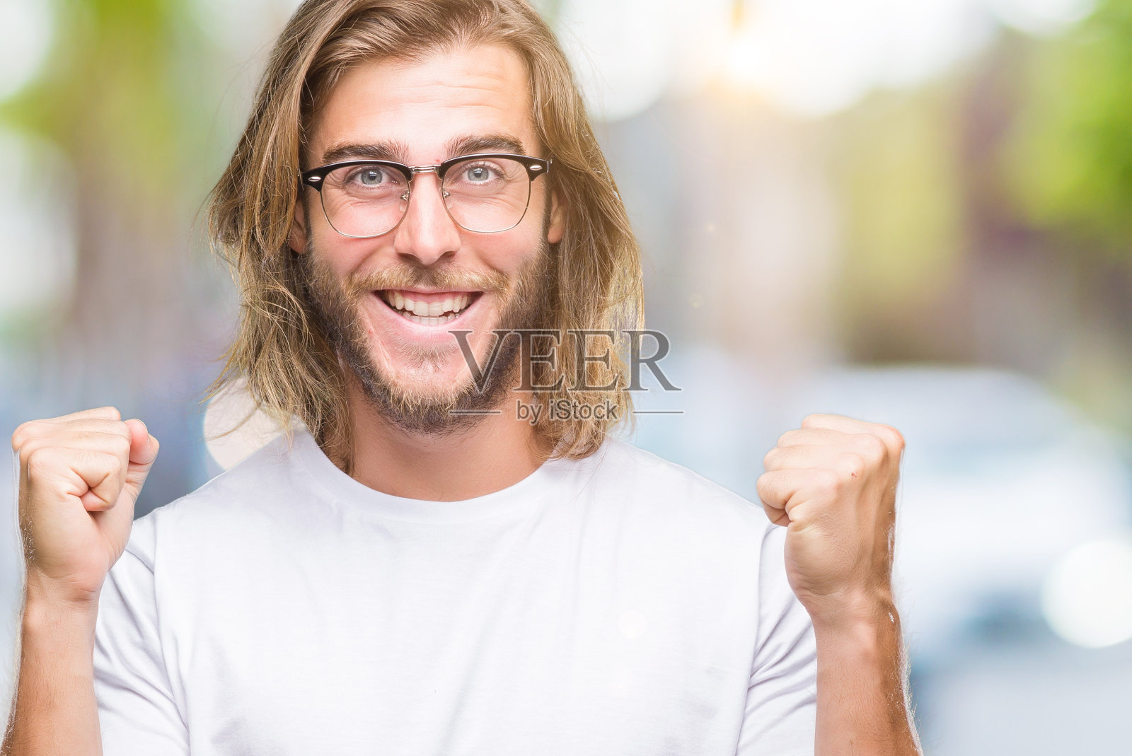 年轻英俊的男人与长头发戴眼镜在孤立的背景庆祝惊讶和惊讶的成功，举起手臂和睁开眼睛。赢家的概念。照片摄影图片
