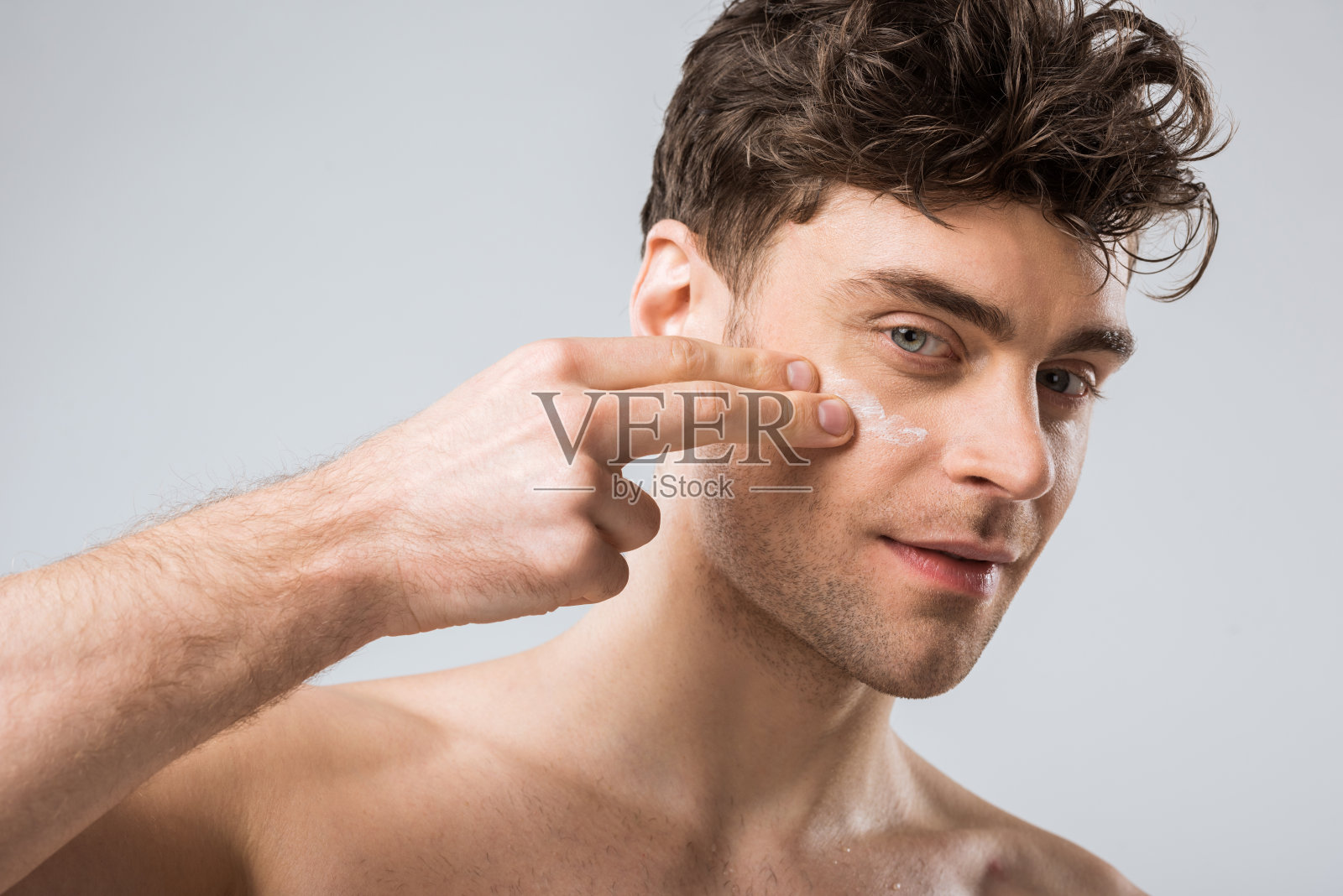 年轻男子在脸上涂抹化妆霜，孤立在灰色照片摄影图片
