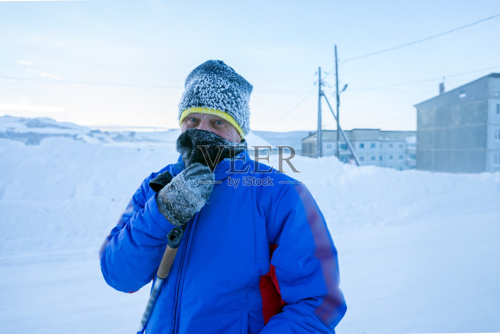 在一个霜冻的日子里，一位男性滑雪者站在住宅楼前面的冬季街道上。照片摄影图片