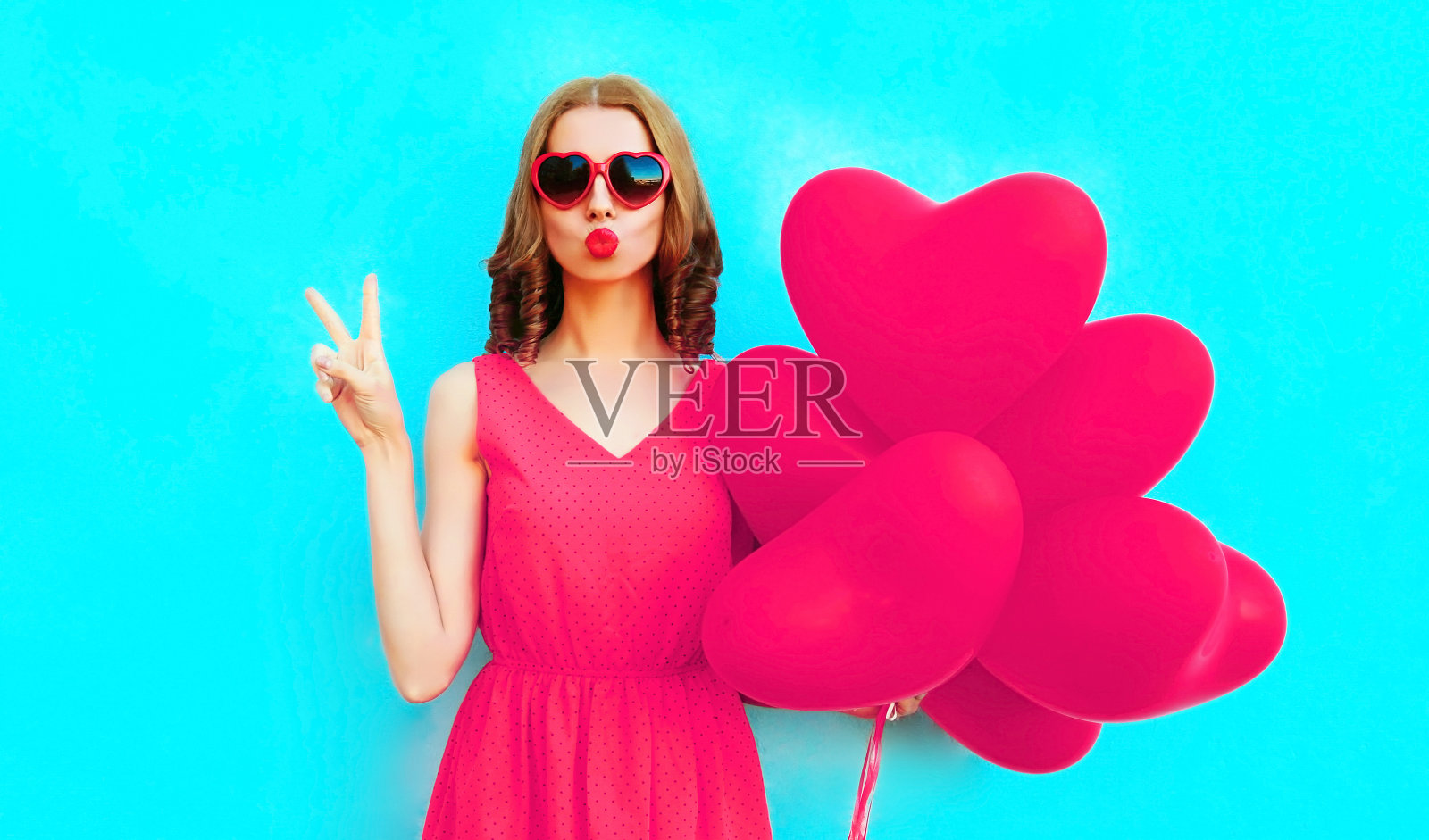 肖像酷女孩与粉色心形气球送甜蜜的空中吻在彩色的蓝色背景照片摄影图片