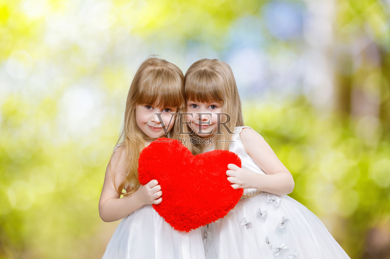 一对双胞胎姐妹抱着红心在一起。照片摄影图片