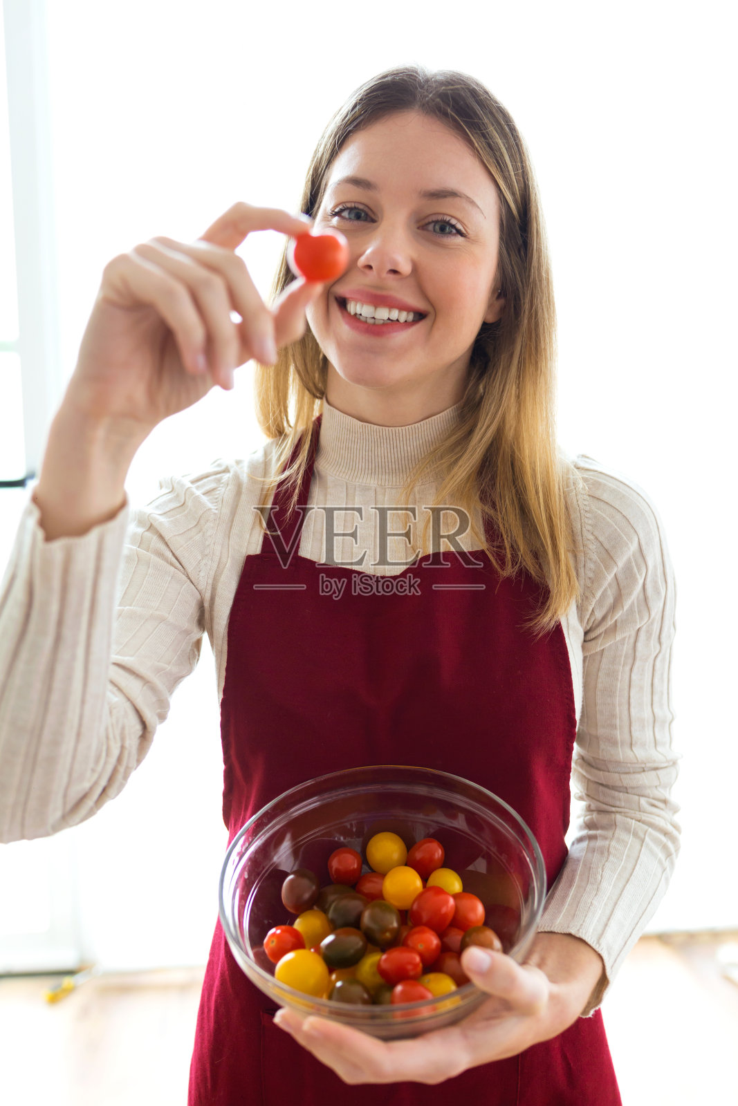 微笑美丽的女子手中拿着不同类型的樱桃番茄在圆碗家里。照片摄影图片
