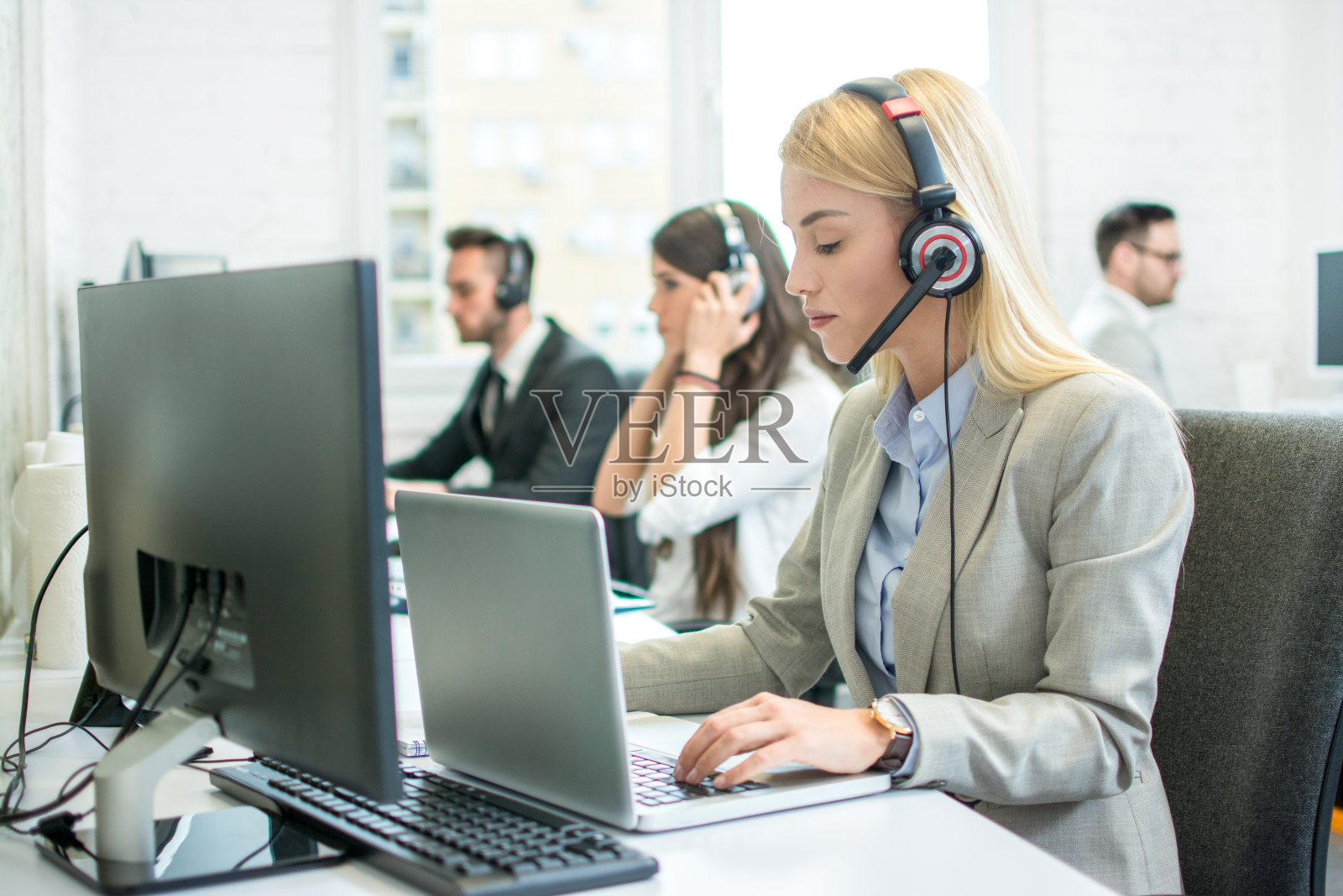 年轻漂亮的女性客户支持操作员，戴着耳机在呼叫中心的笔记本电脑上工作照片摄影图片
