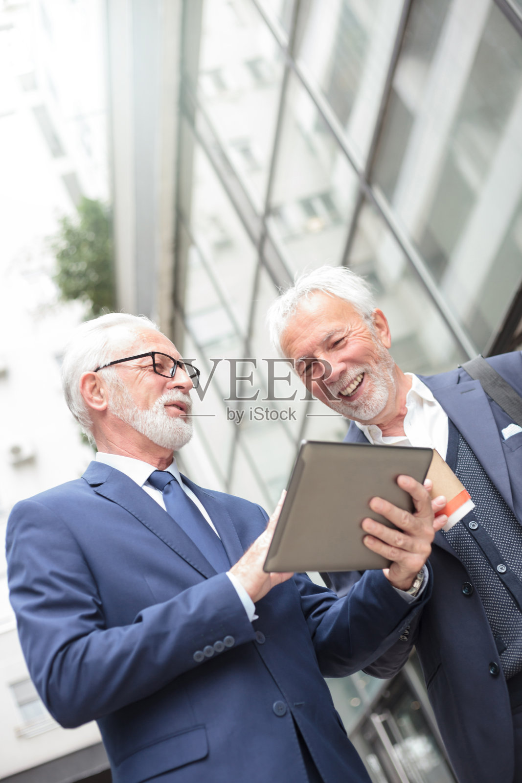 两名面带微笑的资深商人站在一座办公楼前，在平板电脑上工作照片摄影图片