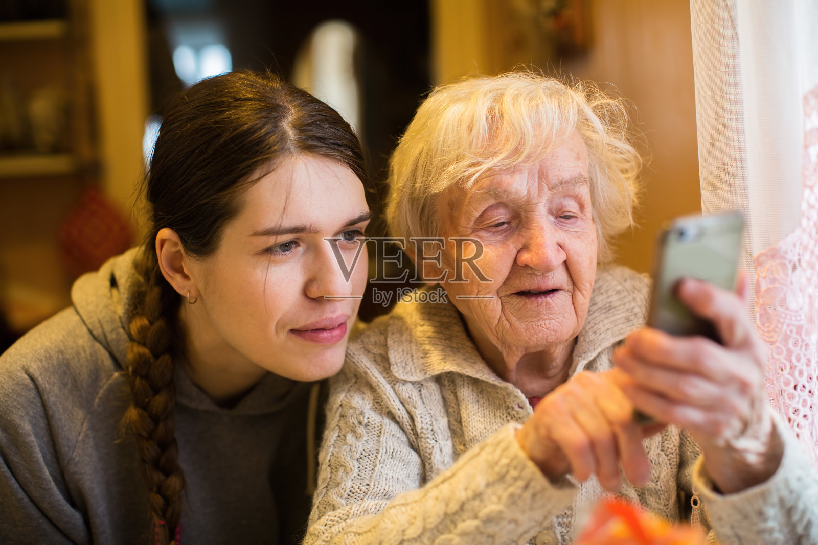 一位年长的妇女和他已经成年的女儿孙女在智能手机上看着并打字。照片摄影图片