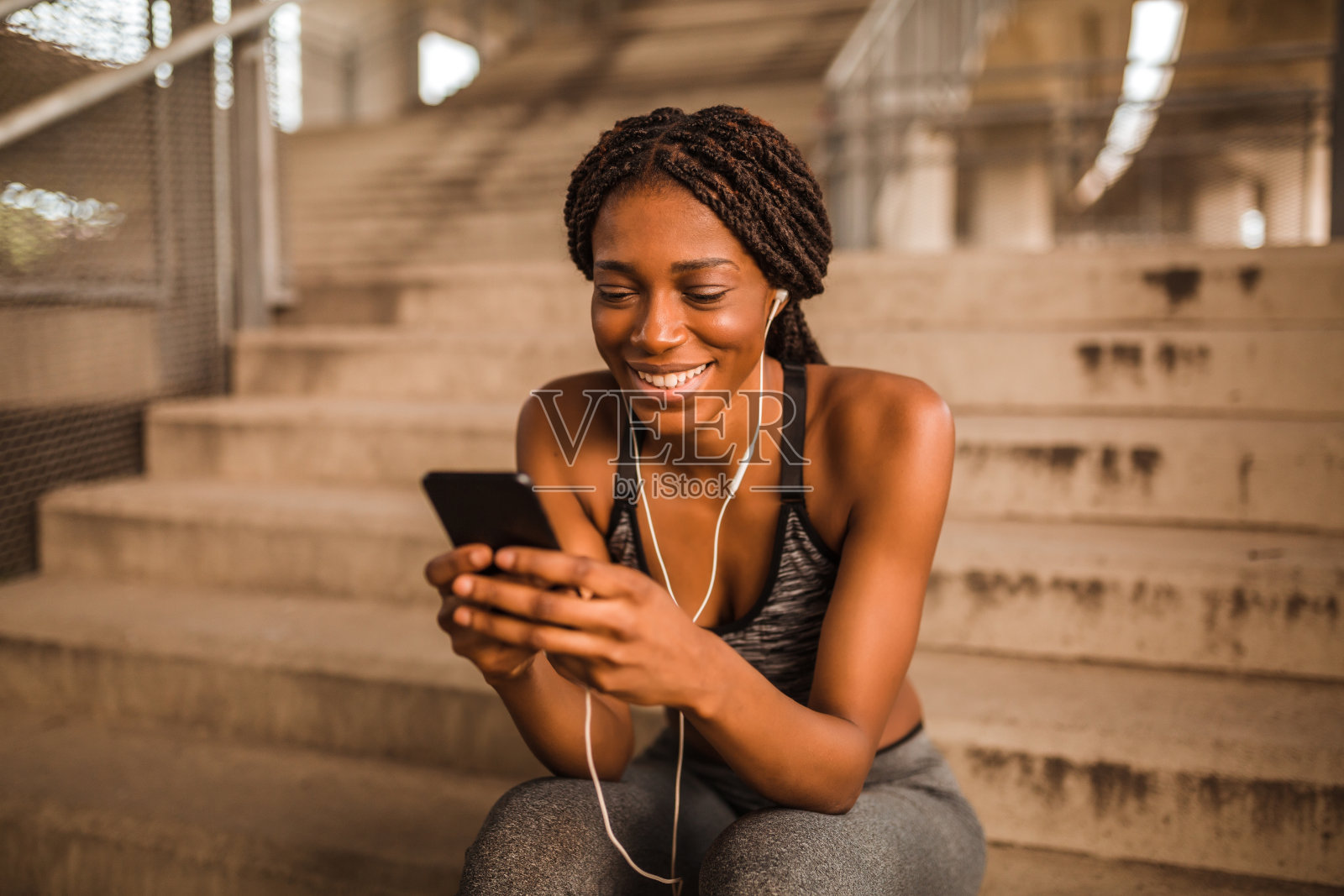 一位年轻的非洲裔美国妇女坐在楼梯上，用耳机听她最喜欢的音乐照片摄影图片