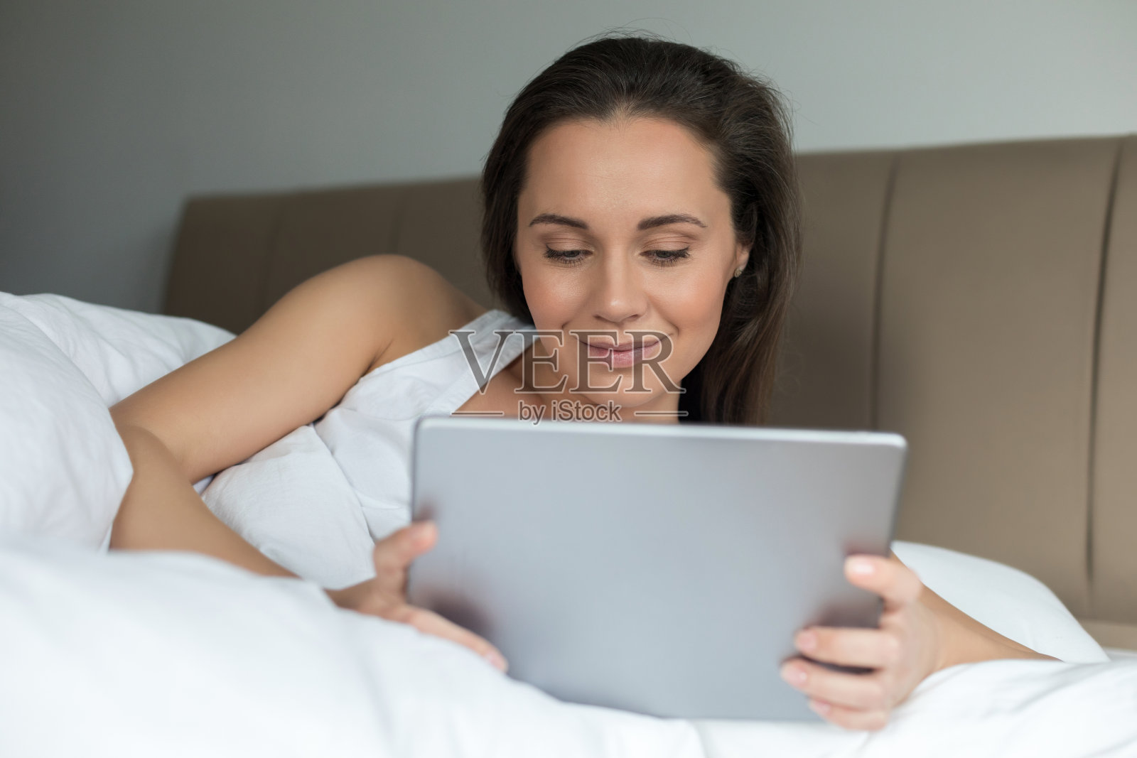 年轻女子在床上使用平板电脑照片摄影图片