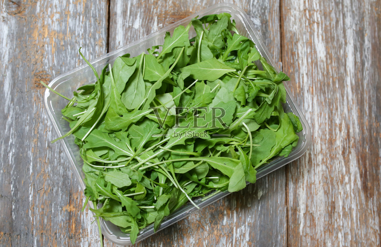 木背景上的塑料盒子里的芝麻菜沙拉。生菜是健康食品。素食主义者的生活方式的概念。绿色新鲜维生素。照片摄影图片