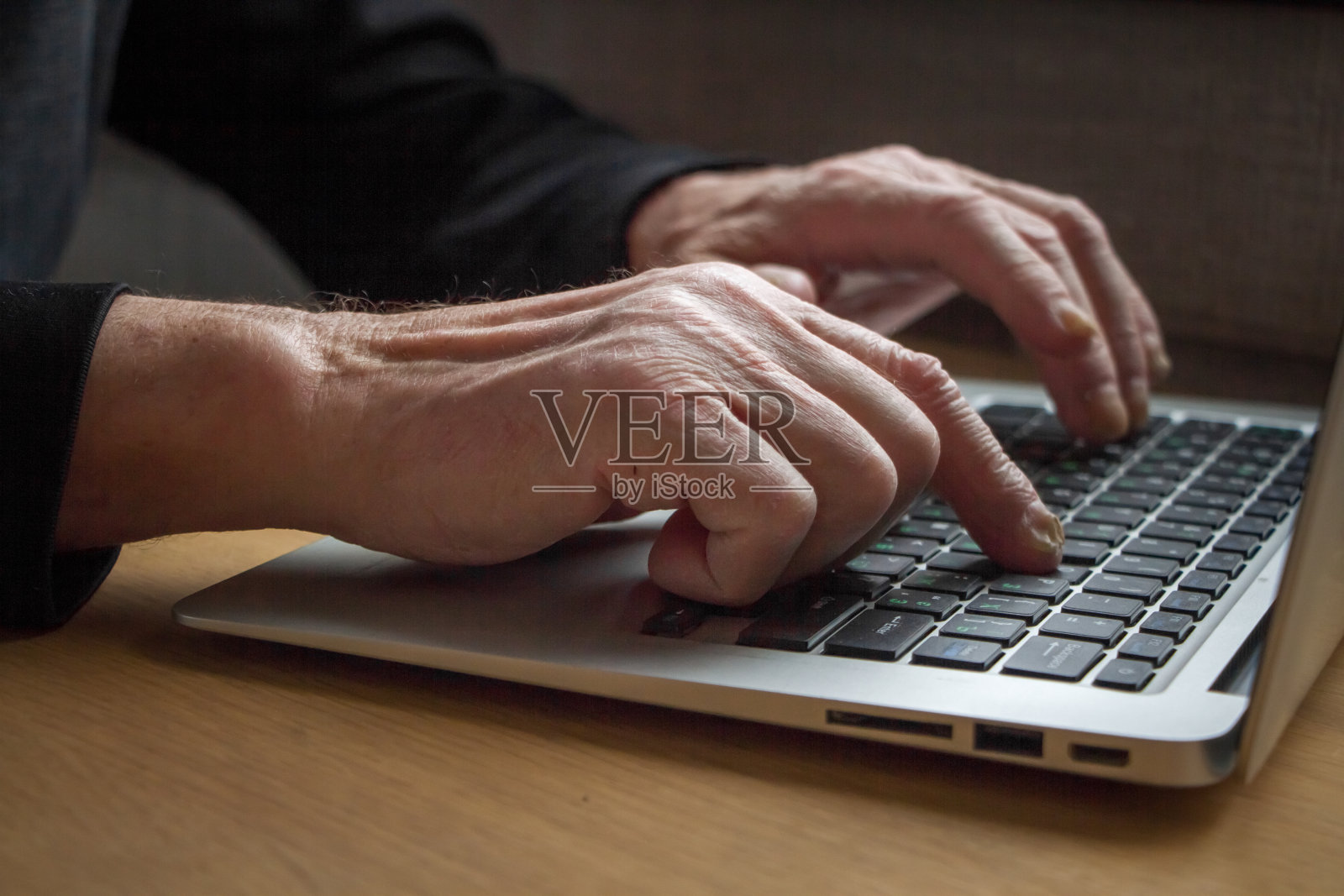一个老人的手在笔记本电脑的键盘上工作，打字，在互联网上搜索信息。照片摄影图片