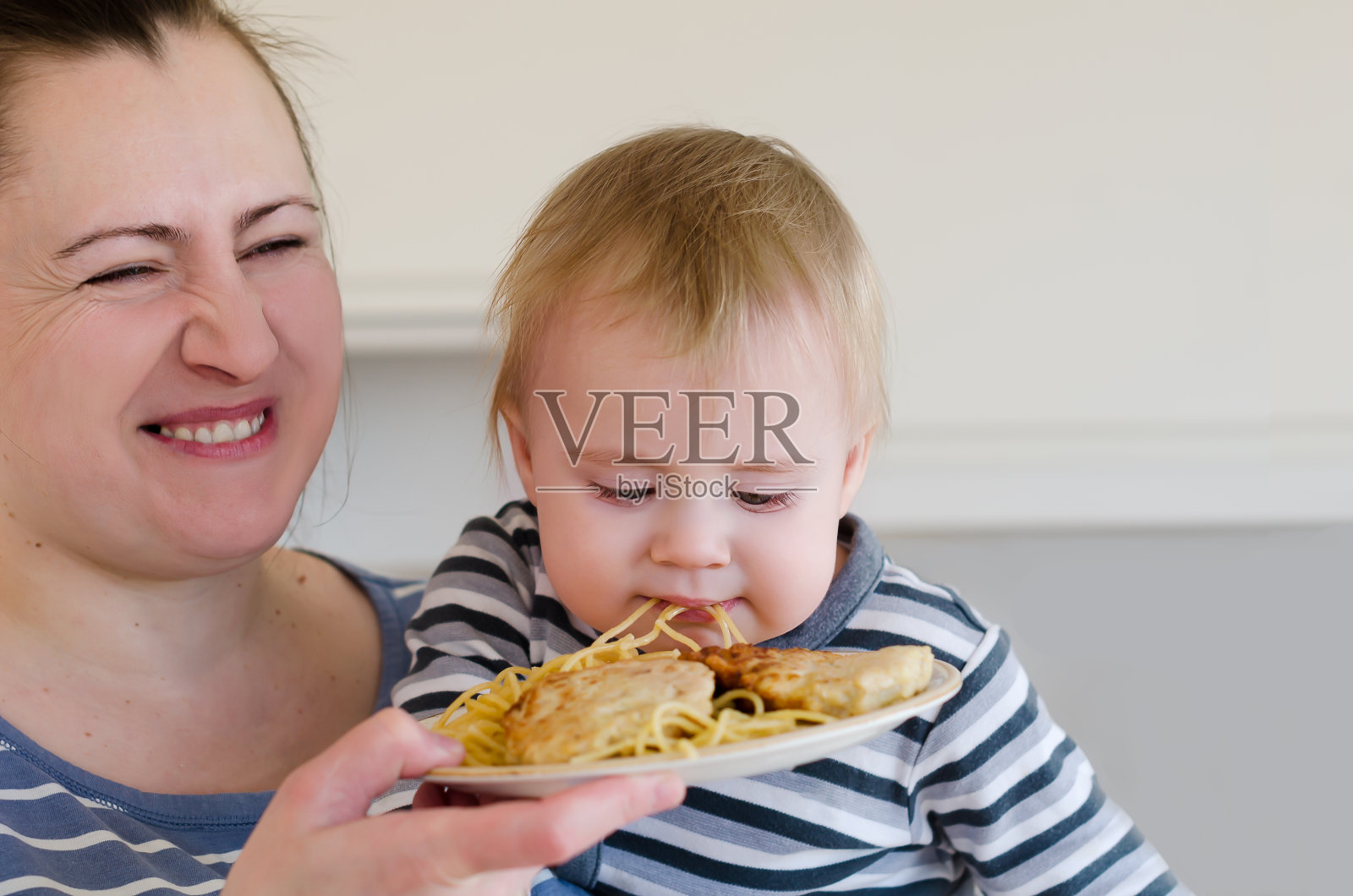 母亲正在用盘子里的正常食物喂小男孩照片摄影图片