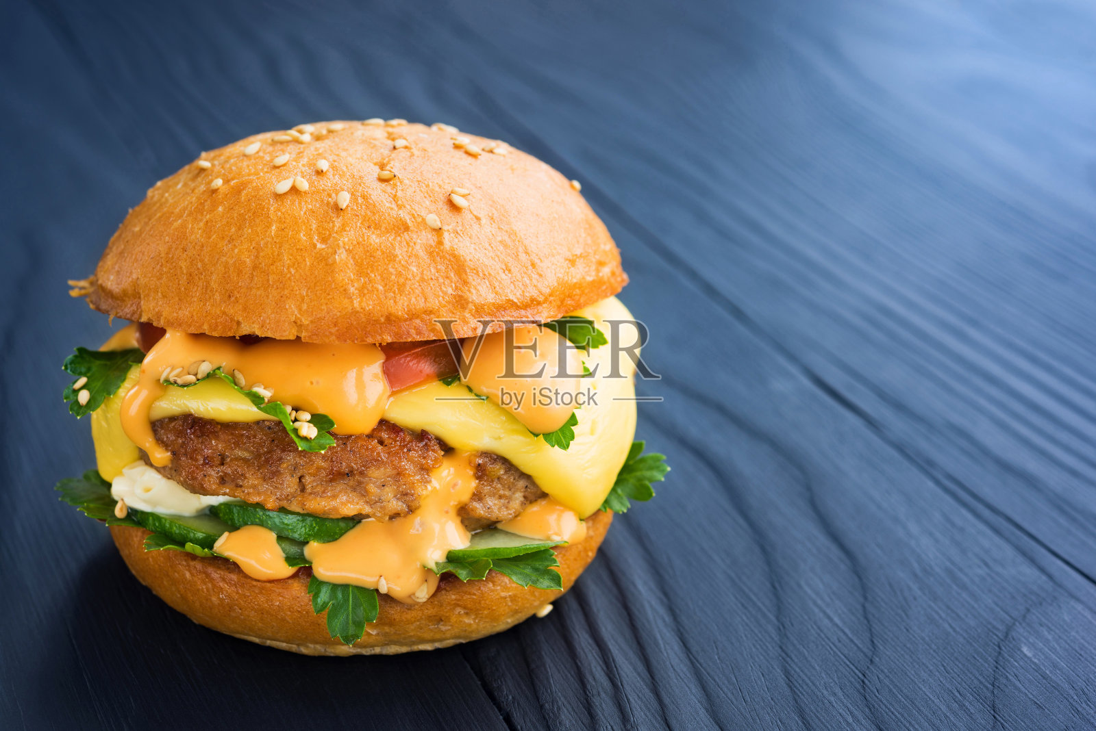 美味的自制汉堡配上西红柿，黄瓜，欧芹，酱汁和奶酪，在一个木制的深色背景。照片摄影图片