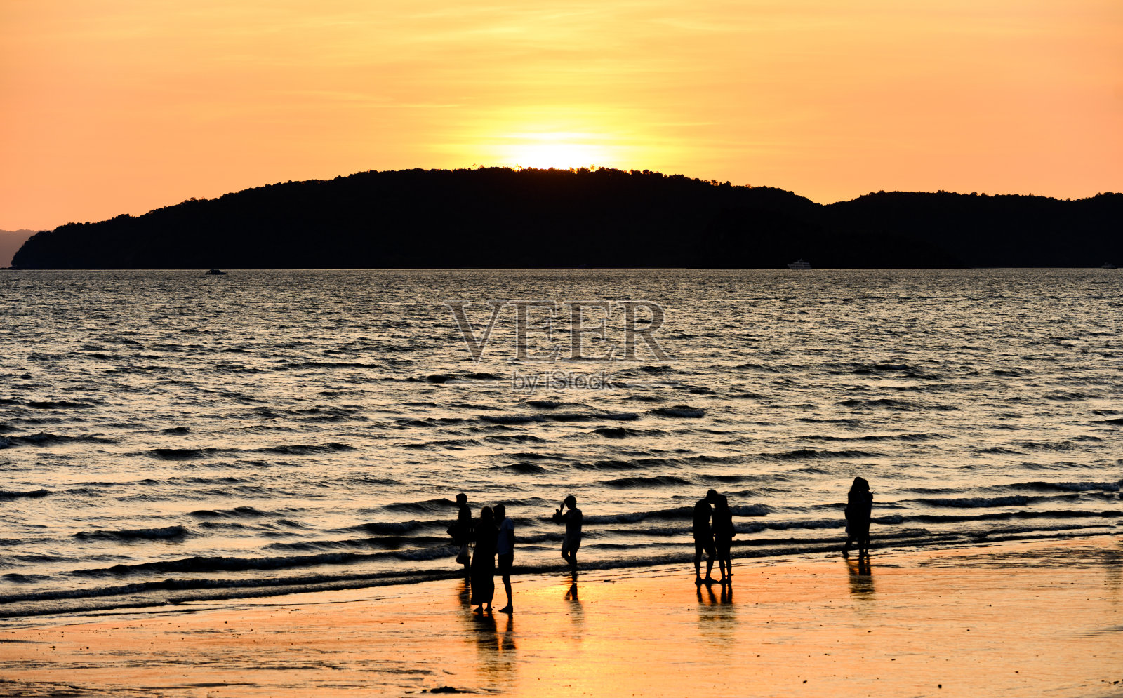 (长曝光)一些不明身份的人模糊的剪影享受令人惊叹的日落在一个美丽的海滩沐浴在一个平静的大海。泰国甲米省奥南海滩。照片摄影图片
