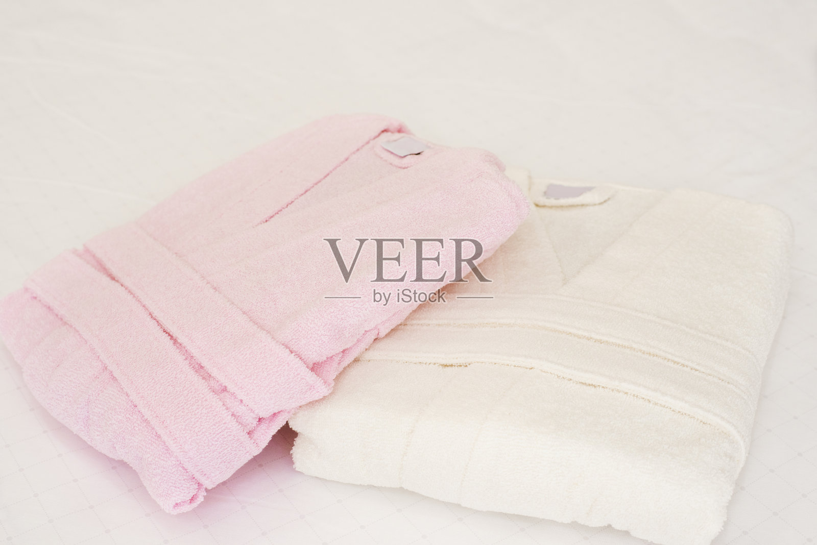 房间床上折叠的浴袍。白色和粉色，两件长袍照片摄影图片