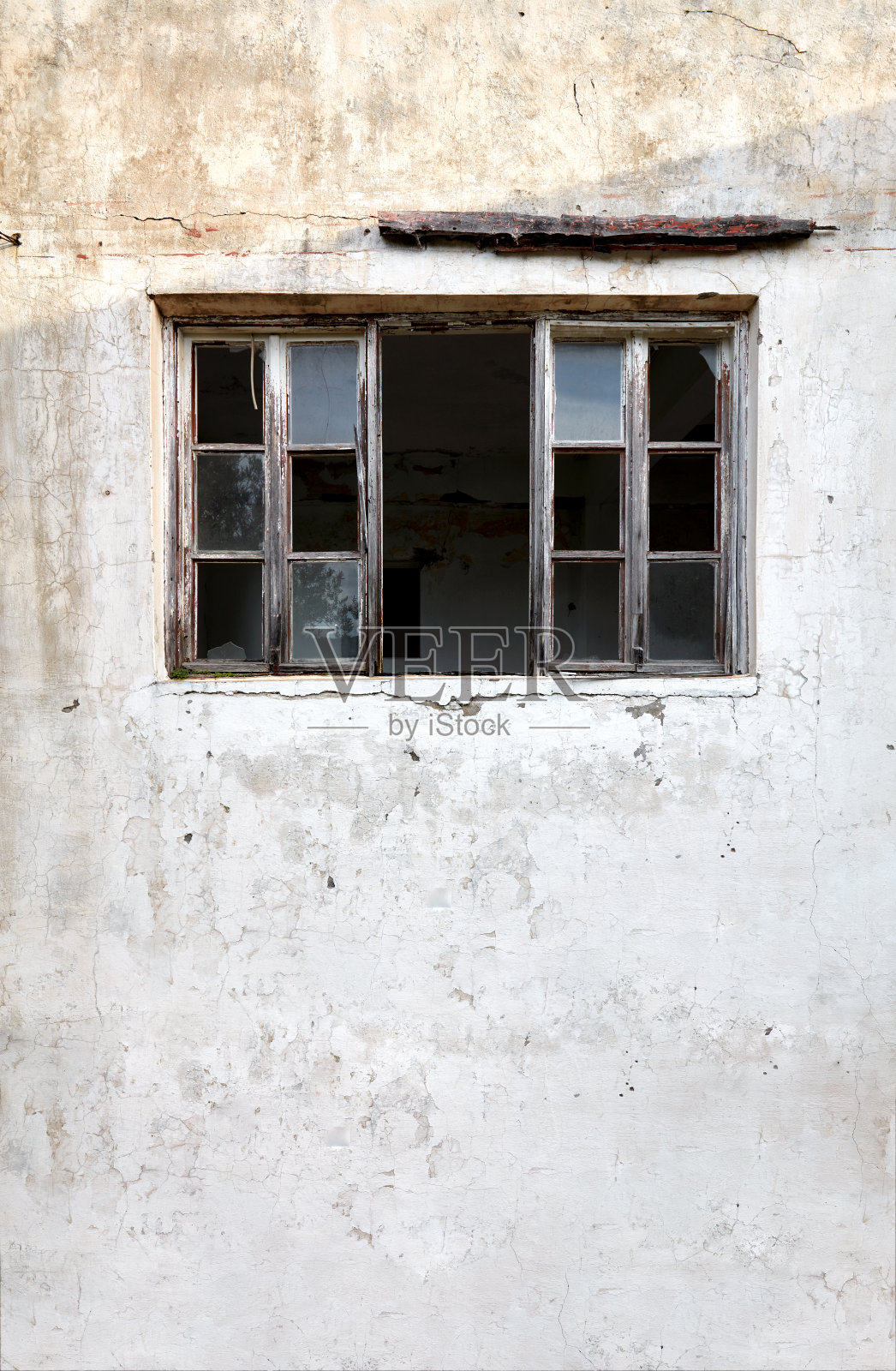 一个废弃的旧小屋的外观，破旧的木窗框和白色的裂缝墙照片摄影图片