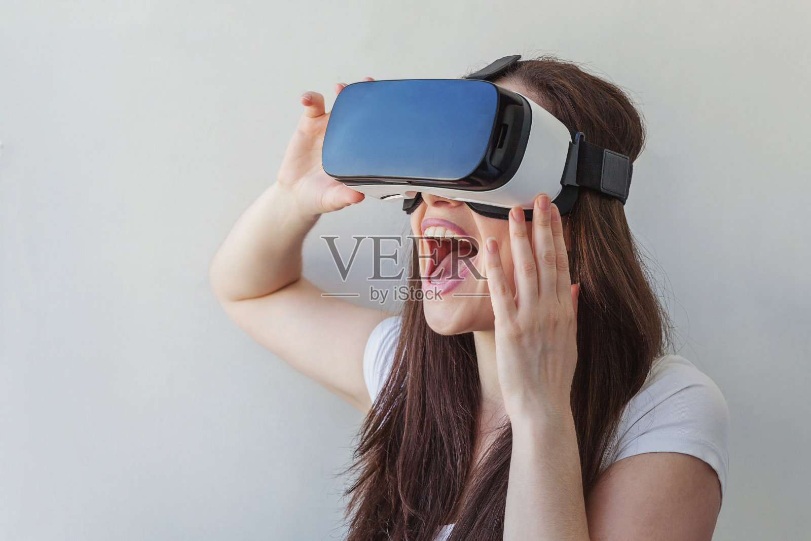 年轻女子戴着使用虚拟现实VR眼镜的微笑头盔头戴在白色背景上照片摄影图片