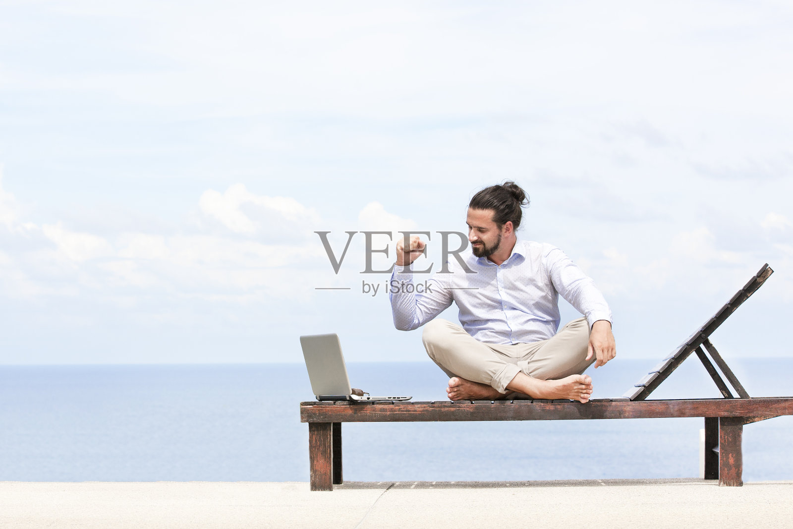 一位年轻的商人正在海滩上的躺椅上休息，他正在使用他的平板电脑照片摄影图片