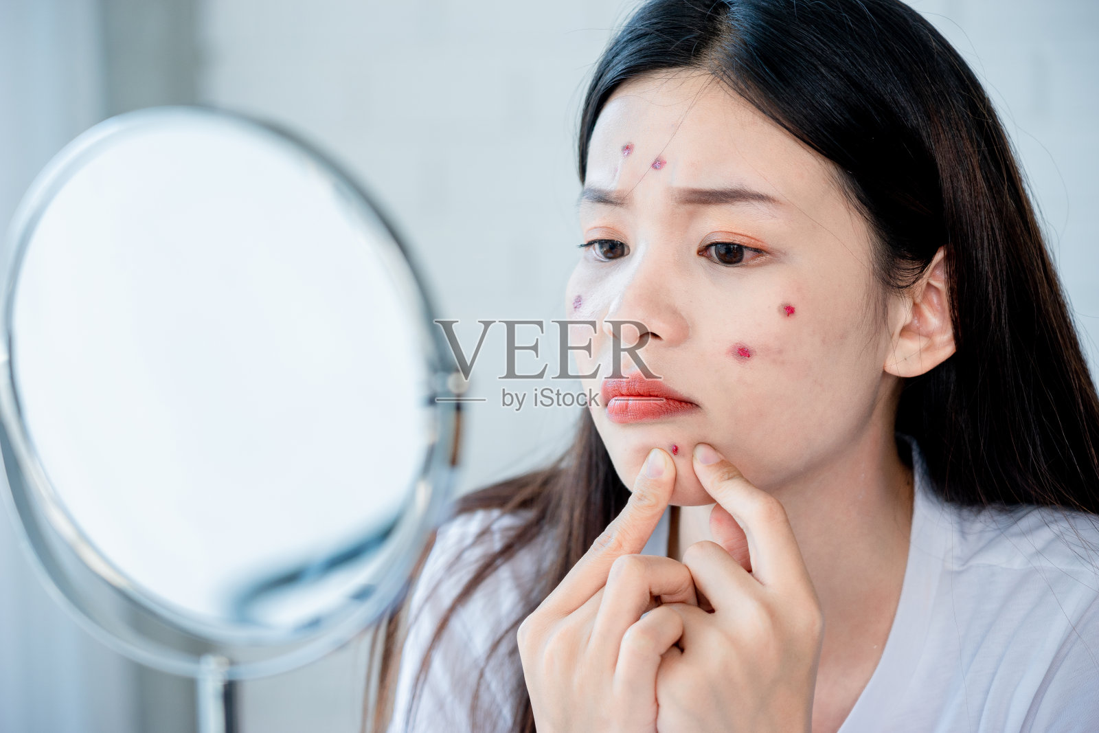 亚洲青少年妇女看着镜子和挤压她脸上的痤疮问题，护肤概念。照片摄影图片