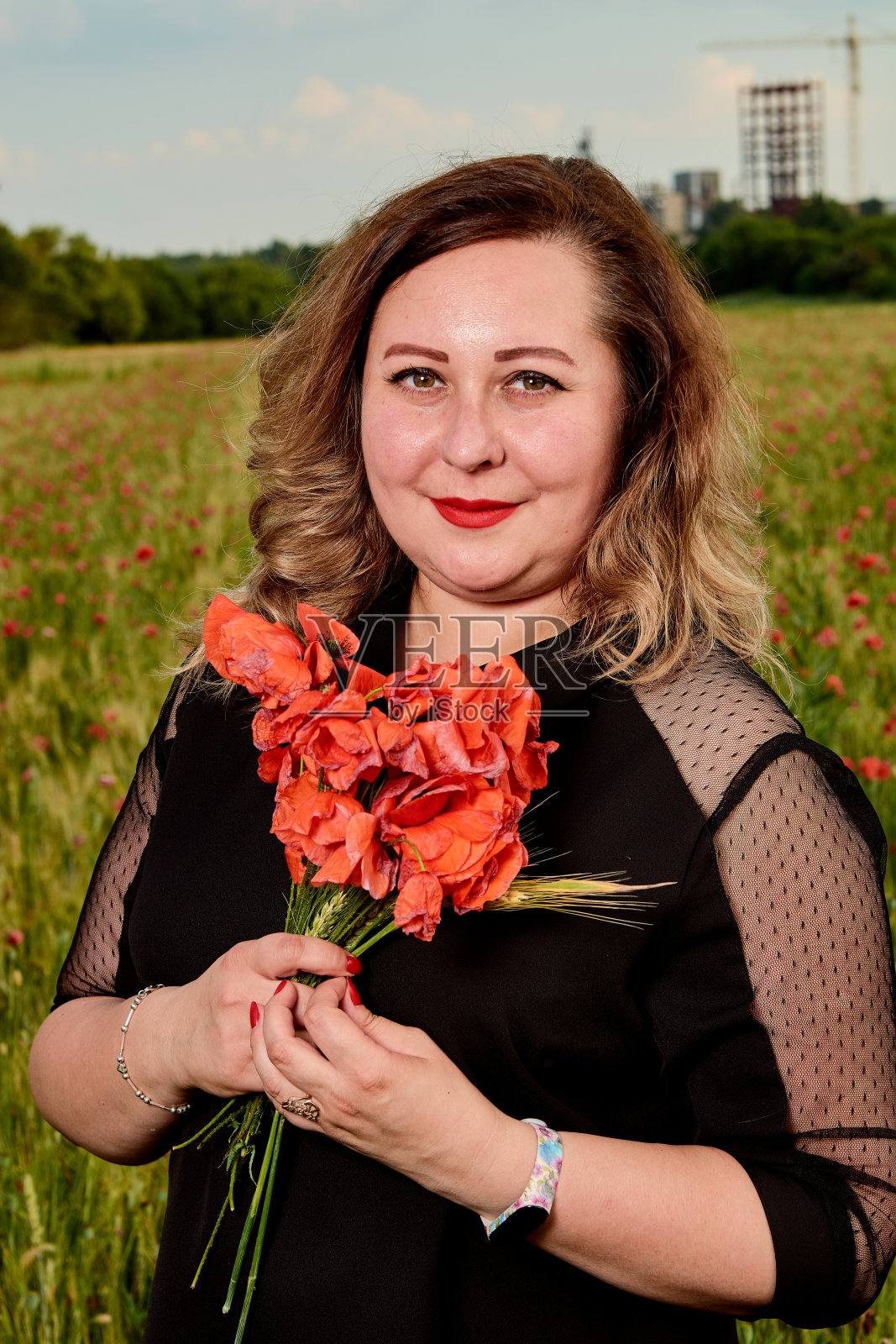 一个穿着黑色裙子的胖女人站在绿色的小麦和野罂粟地里。超重的胖女人。照片摄影图片