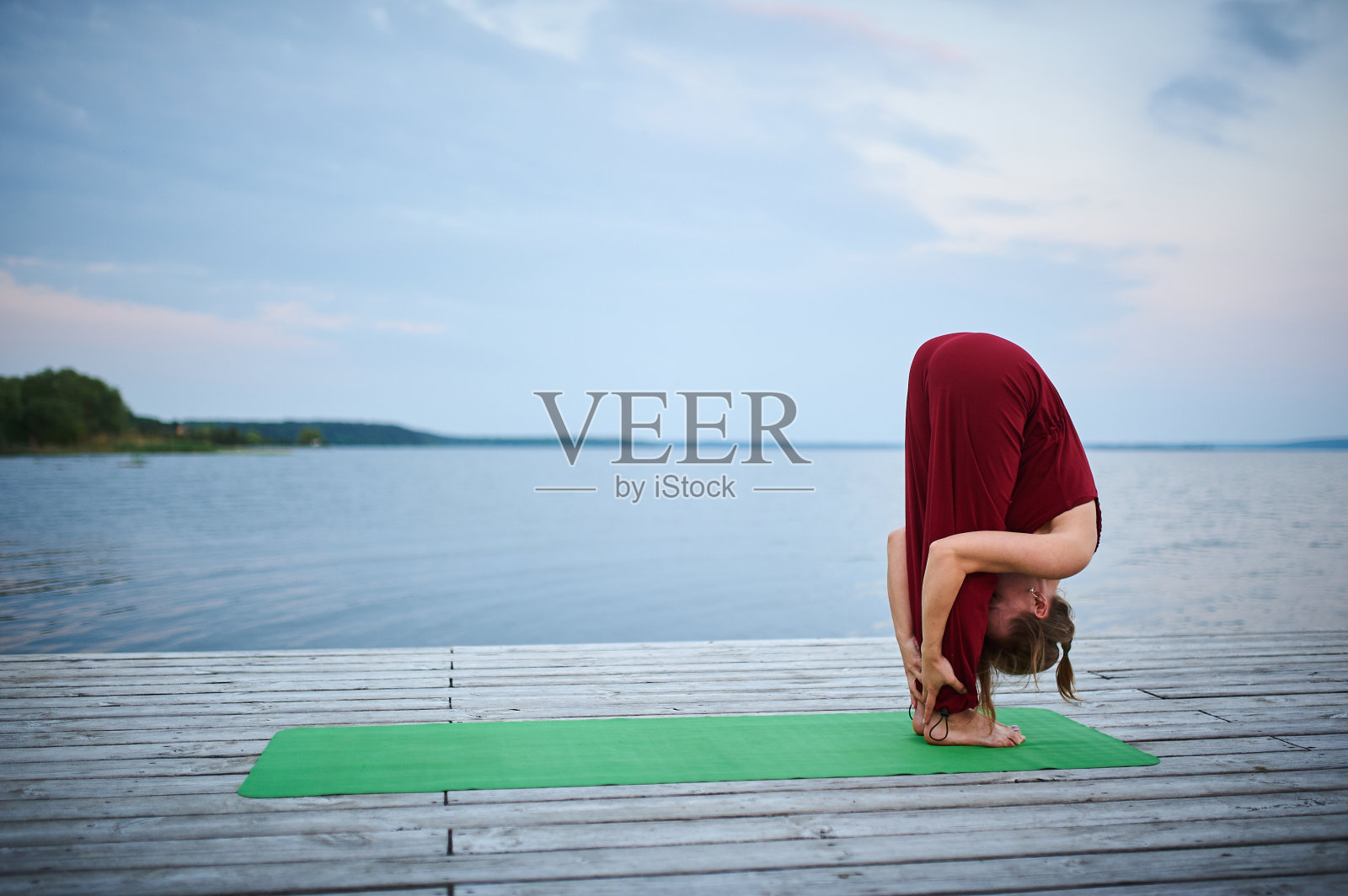 美丽的年轻女子练习瑜伽体式Uttanasana -站立前折叠在木甲板附近的湖照片摄影图片