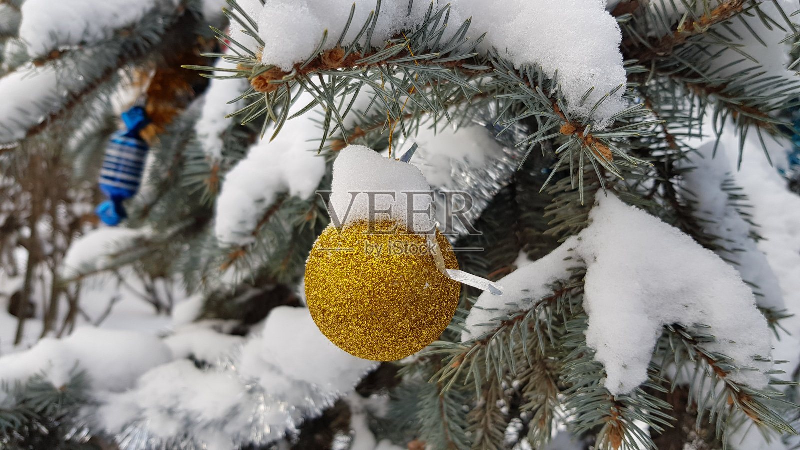 金光闪闪的球圣诞装饰品挂在白雪覆盖的冷杉树枝下。积雪的针叶树纹理。寒假户外场景。新年庆祝背景照片摄影图片