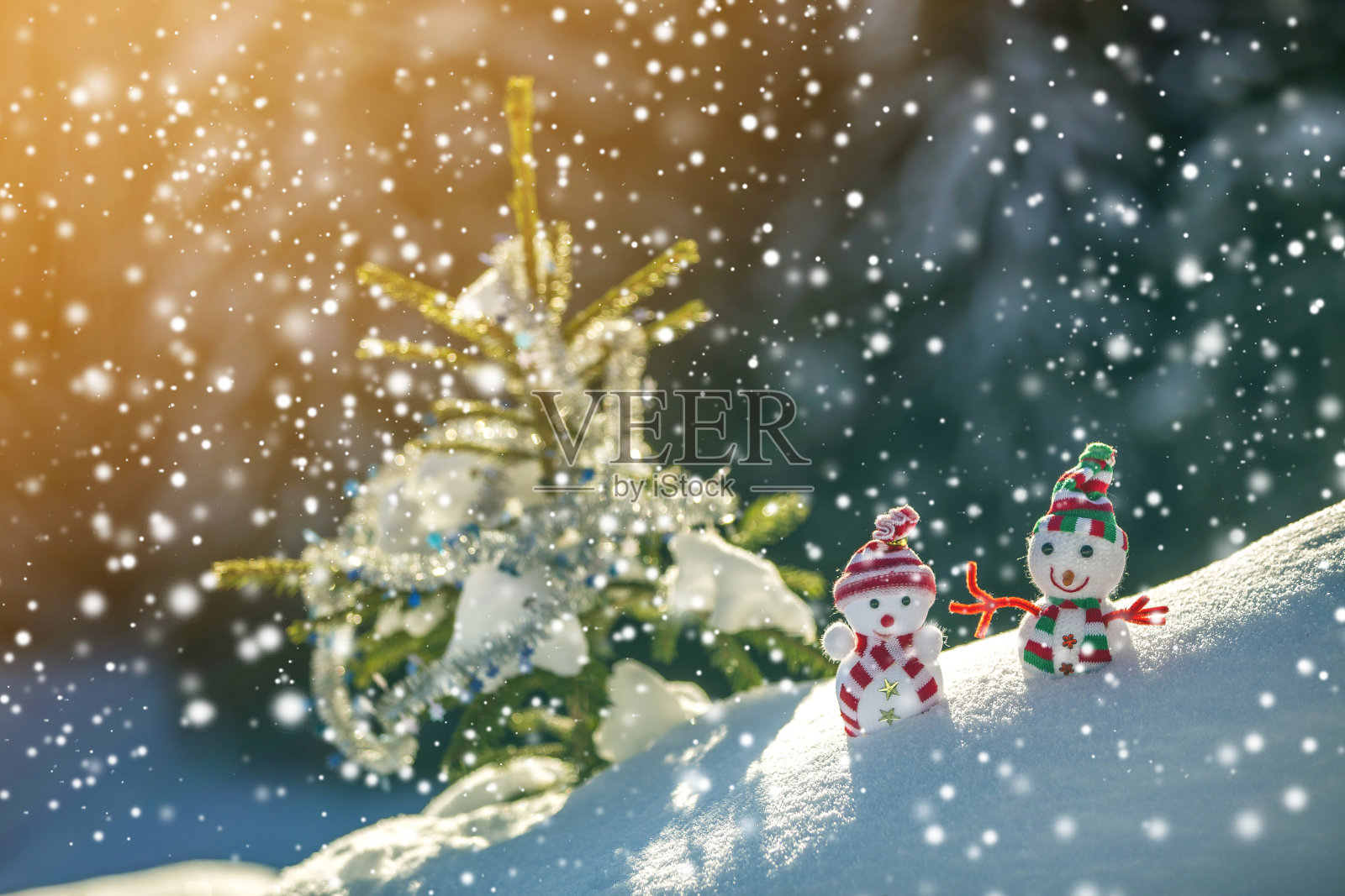 两个有趣的小玩具娃娃雪人在编织的帽子和围巾在深雪户外附近的松树树枝。新年快乐，并附上圣诞贺卡。插画图片素材
