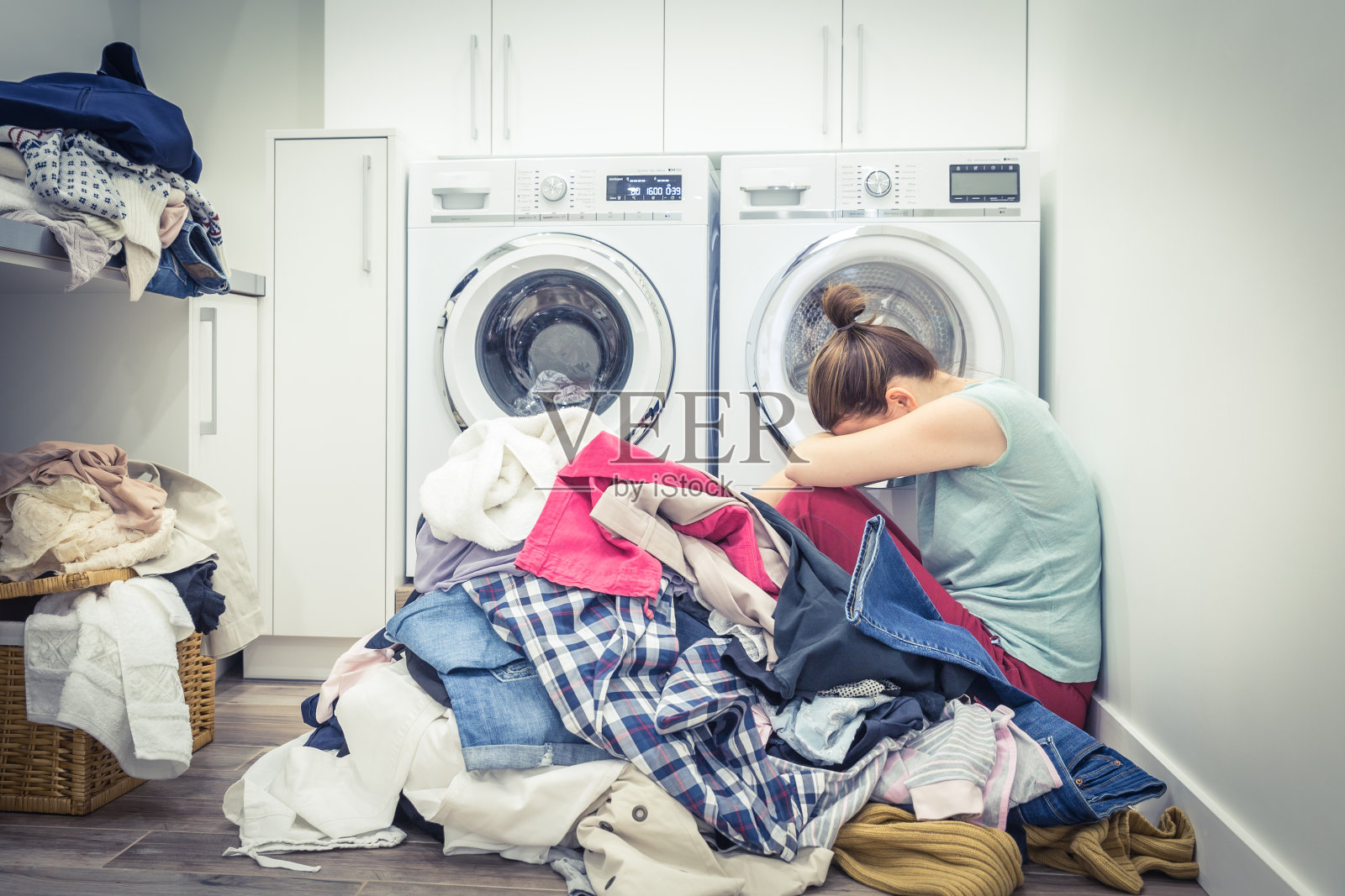 不快乐压力大的女人，在洗衣房的洗衣机旁边堆着一堆衣服，蓝色调照片摄影图片