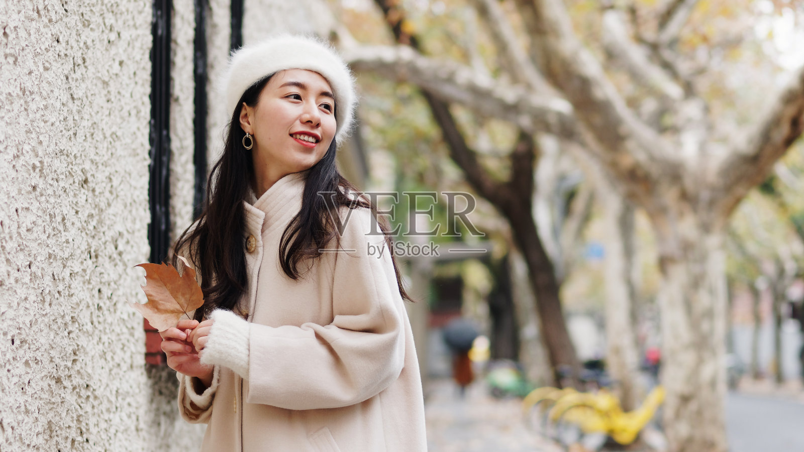 美丽的年轻女子在白色贝雷帽和羊毛衫摆姿势与模糊的街道背景。户外时尚写真魅力中国年轻开朗时尚淑女，街头摄影。照片摄影图片