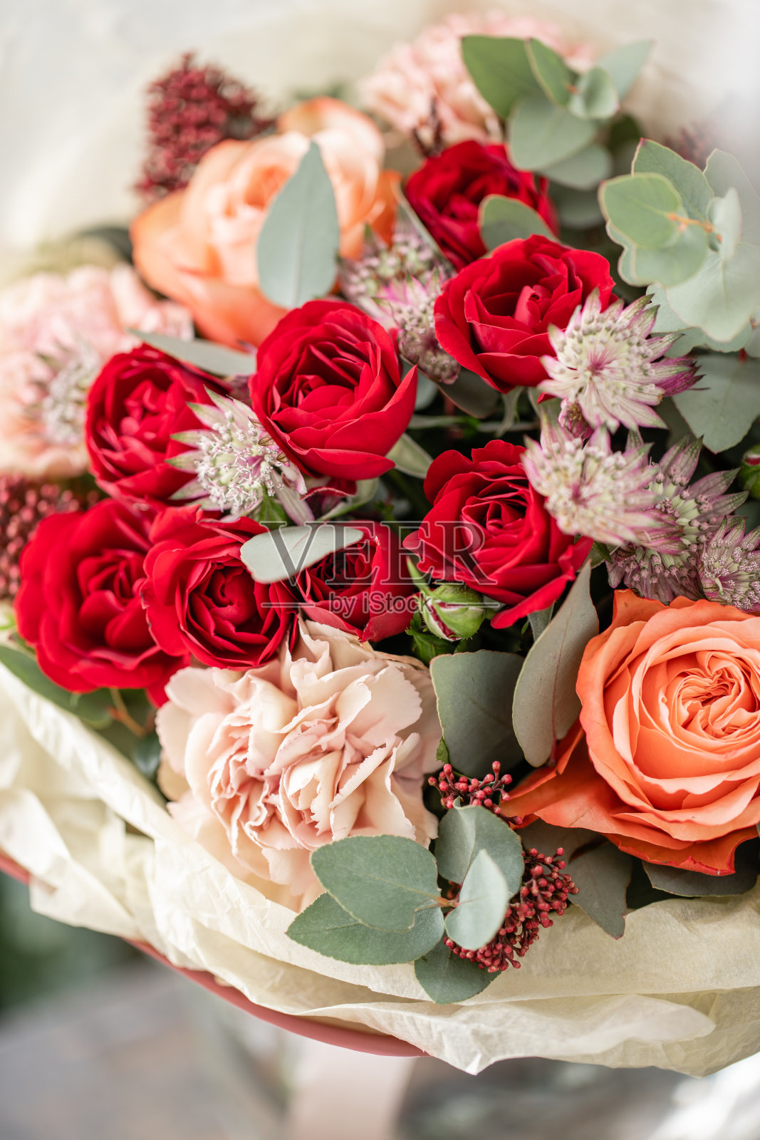 木桌上的花瓶里插着一束漂亮的鲜花。花店花匠的工作。红色的玫瑰和其他花照片摄影图片