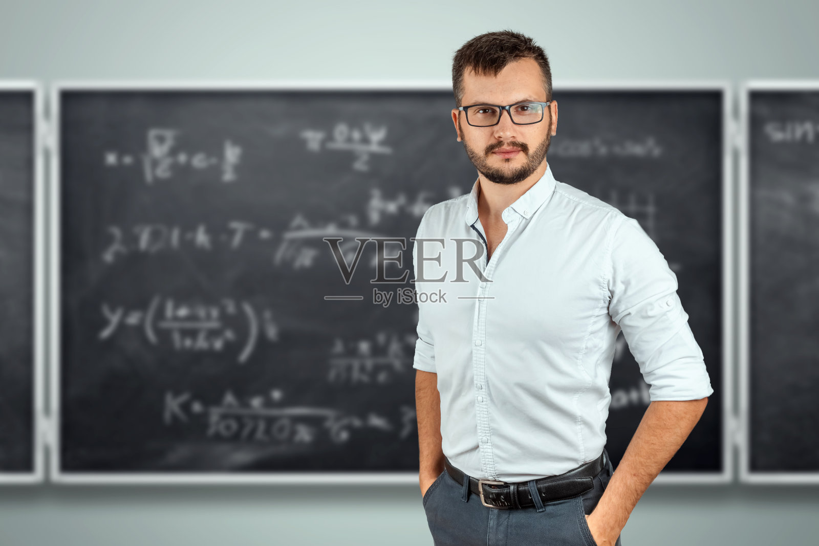 学校黑板背景上的一位年轻男老师的肖像。教师节知识日回学校学习在线学习。照片摄影图片