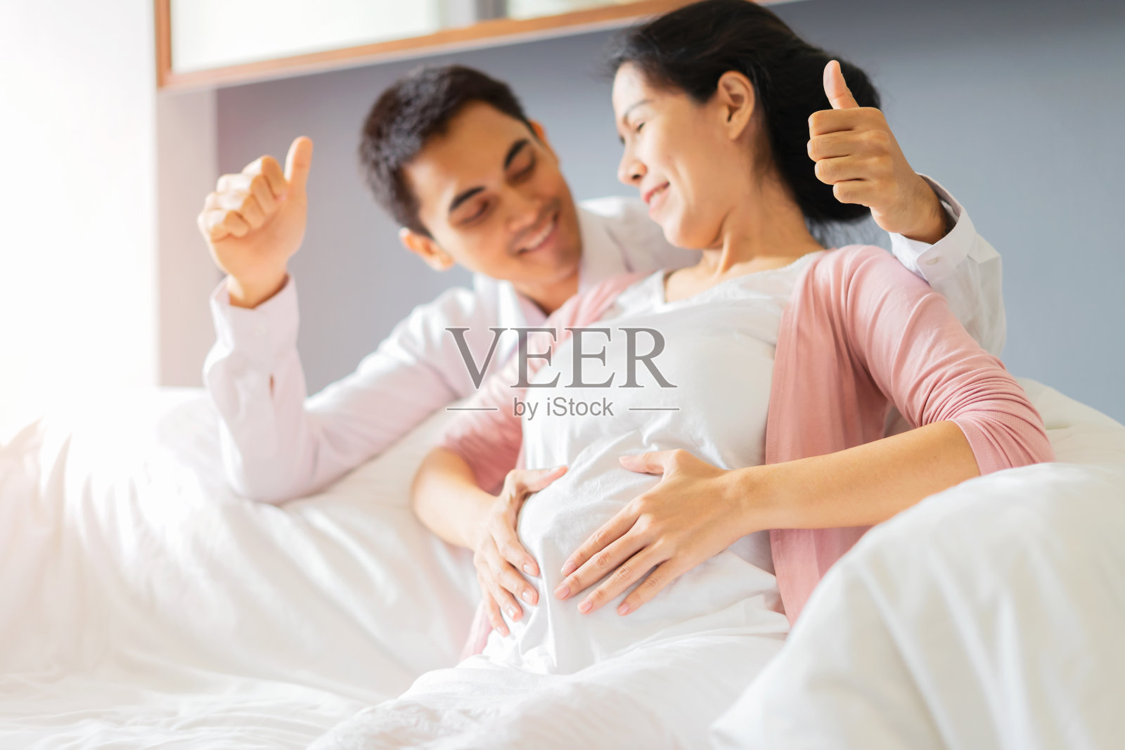 一对年轻的积极夫妇在起居室的沙发上触摸着微笑的孕妇的肚子照片摄影图片