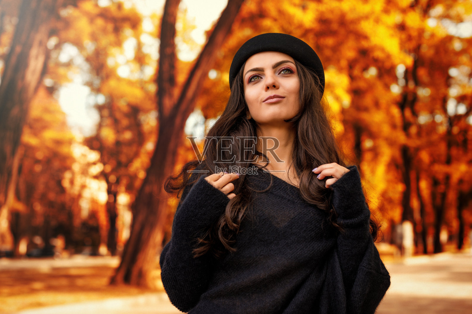 秋叶背景上戴黑帽子的女人。照片摄影图片
