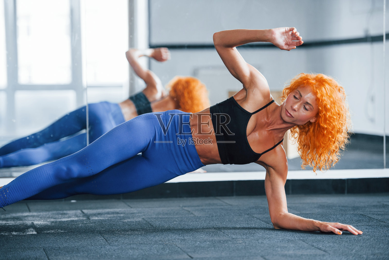 对镜子。喜欢运动的红发女孩白天去健身房健身。肌肉发达的身体类型照片摄影图片