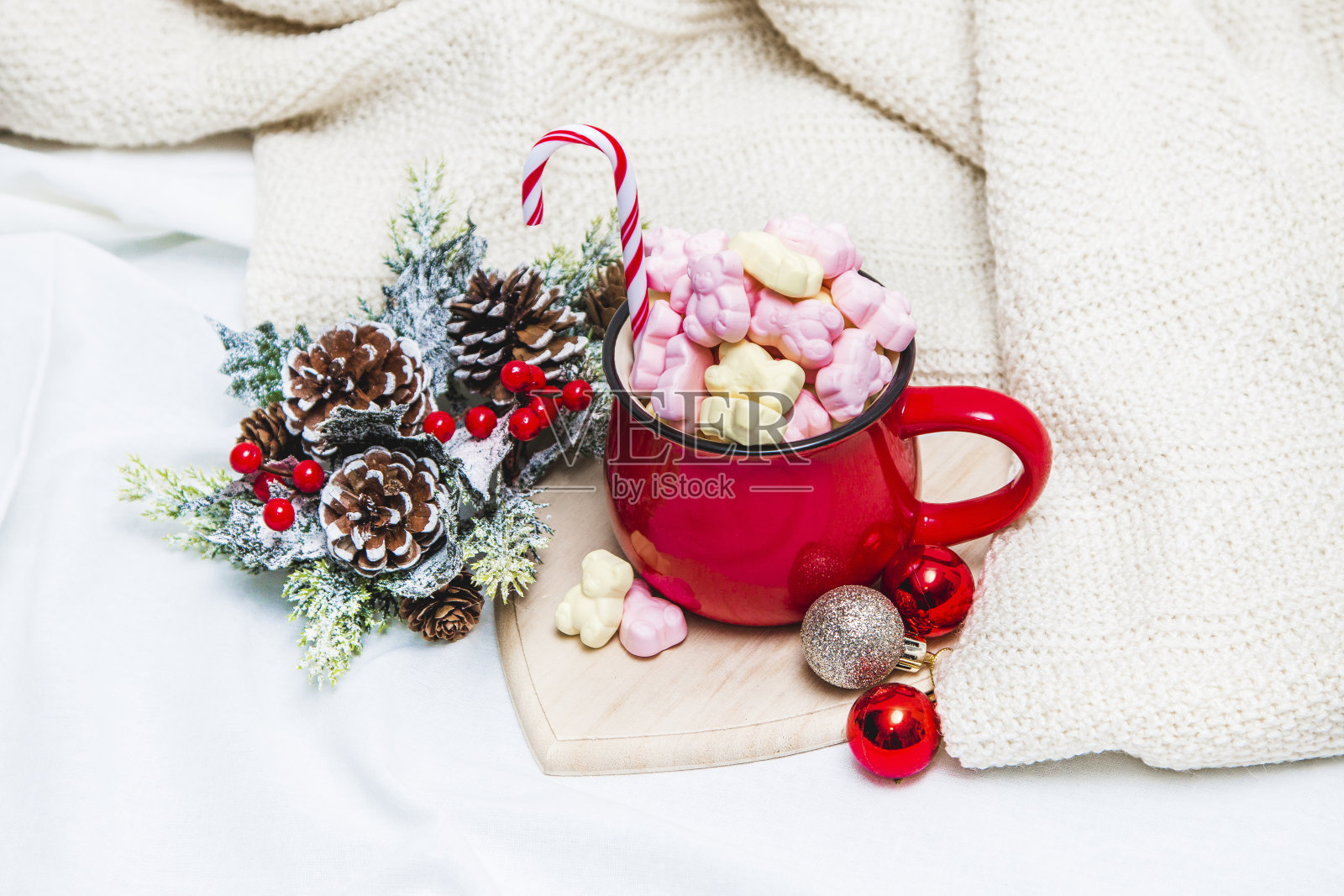 白色床单上放着棉花糖和冬季装饰品的红色杯子照片摄影图片