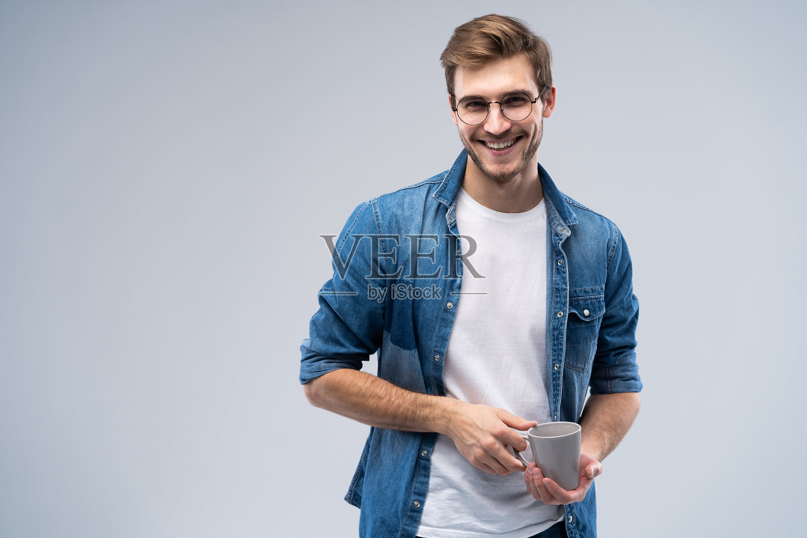 英俊微笑的男人与一杯咖啡孤立在灰色的背景。照片摄影图片