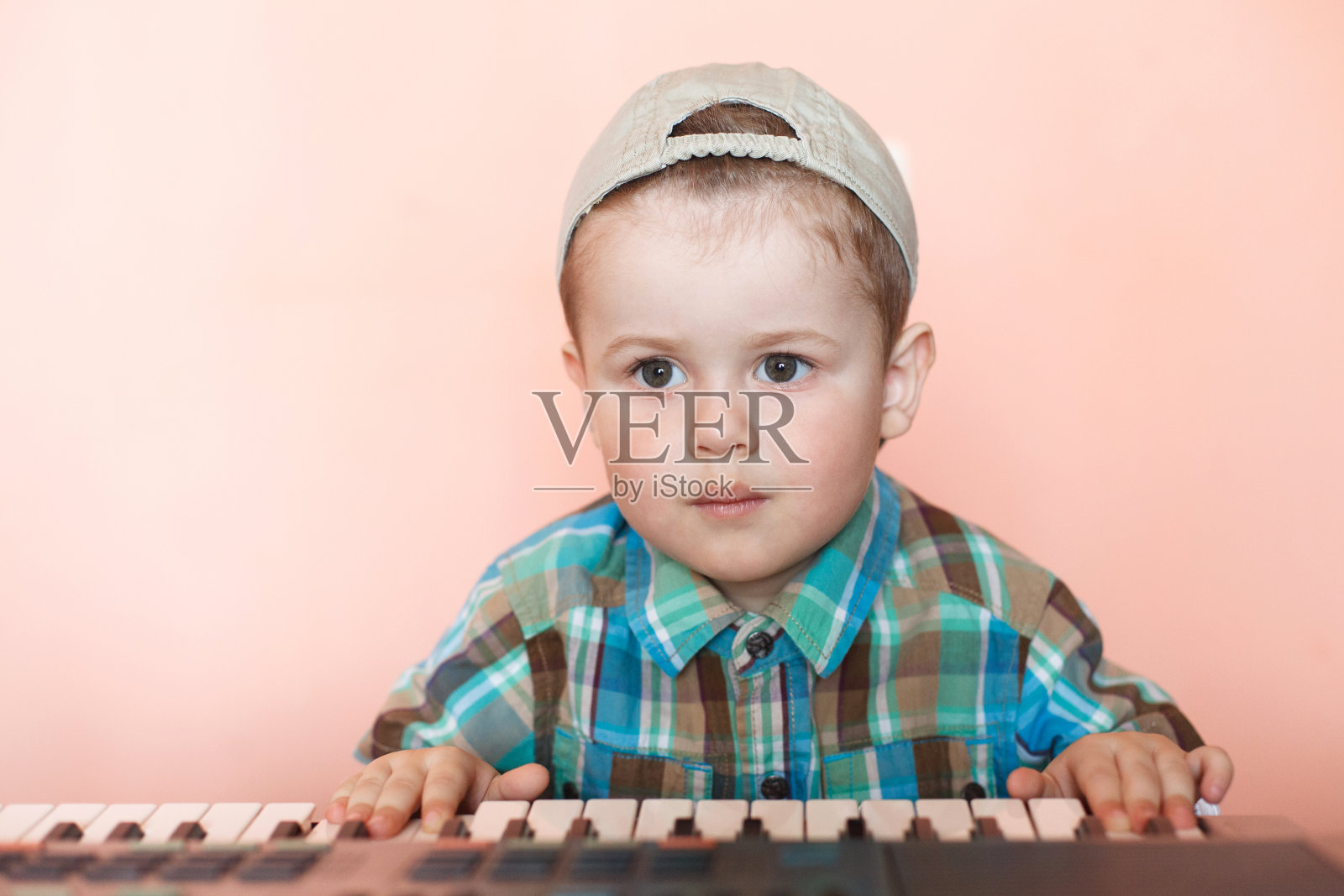 一个漂亮的男孩戴着棒球帽倒着弹数字钢琴。照片摄影图片