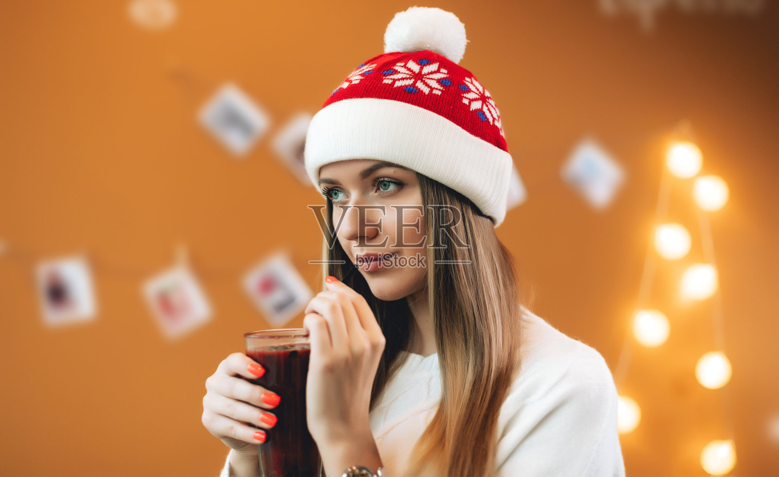 圣诞节的心情。年轻美丽的女孩戴着圣诞帽和白色毛衣享受一杯饮料照片摄影图片
