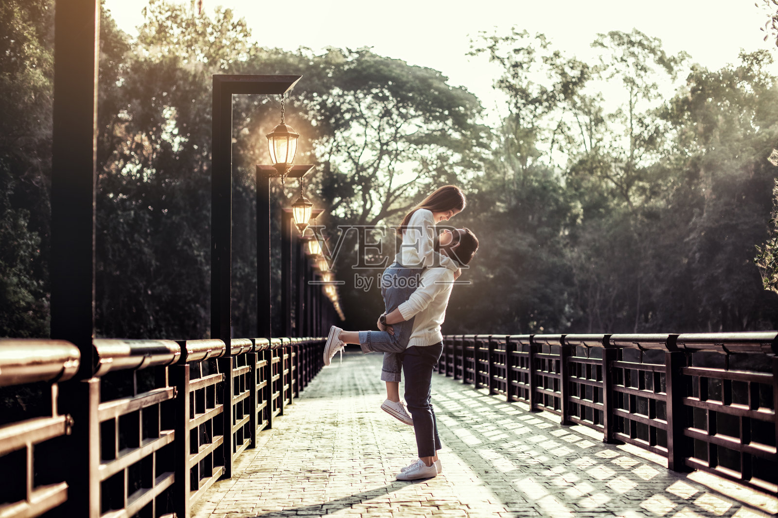 那个强壮的亚洲男人一路拿着灯在桥上扶着他的女朋友。背景是森林。照片摄影图片