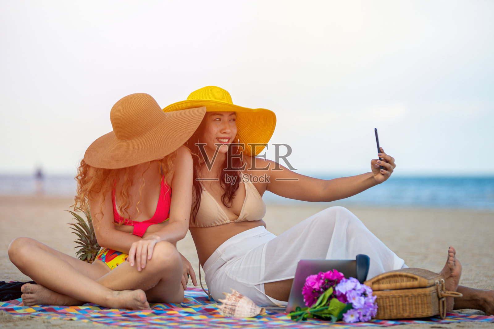 夏天，女人和朋友们在沙滩上拍照自拍。照片摄影图片
