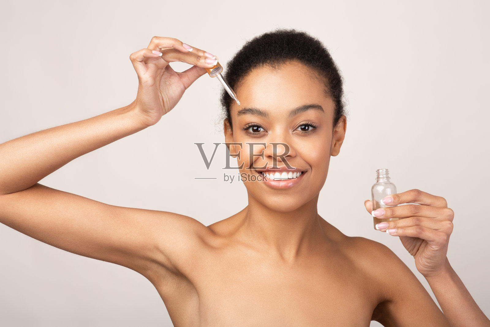 非裔美国女孩在脸上涂抹化妆油，米色背景照片摄影图片